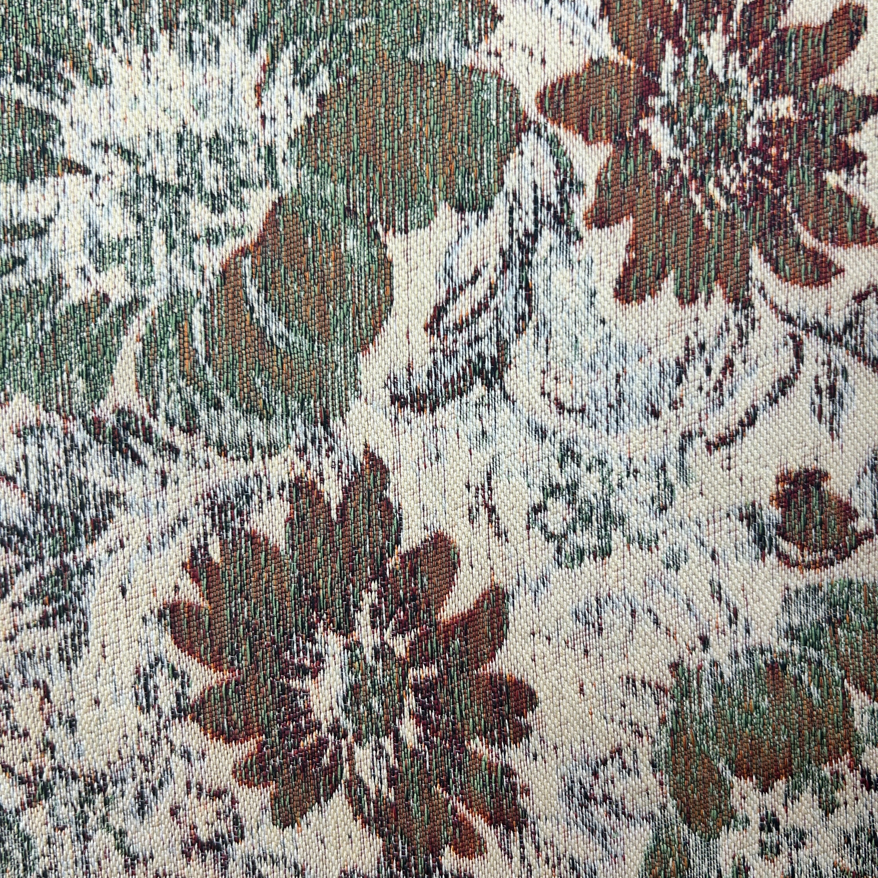 A close-up of a woven fabric with a distressed floral pattern in muted green, brown, and gray on an off-white background.