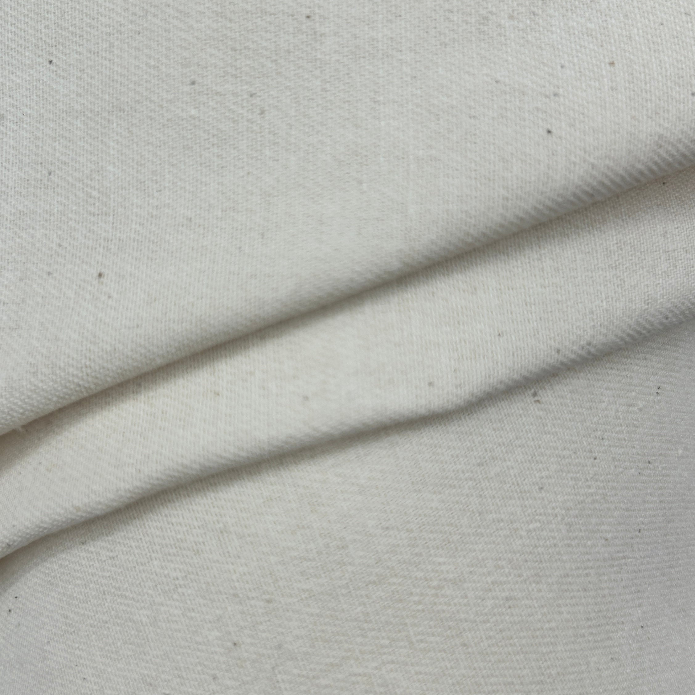 Close-up of folded natural white plain calico canvas heavy fabric with a rustic weave texture.