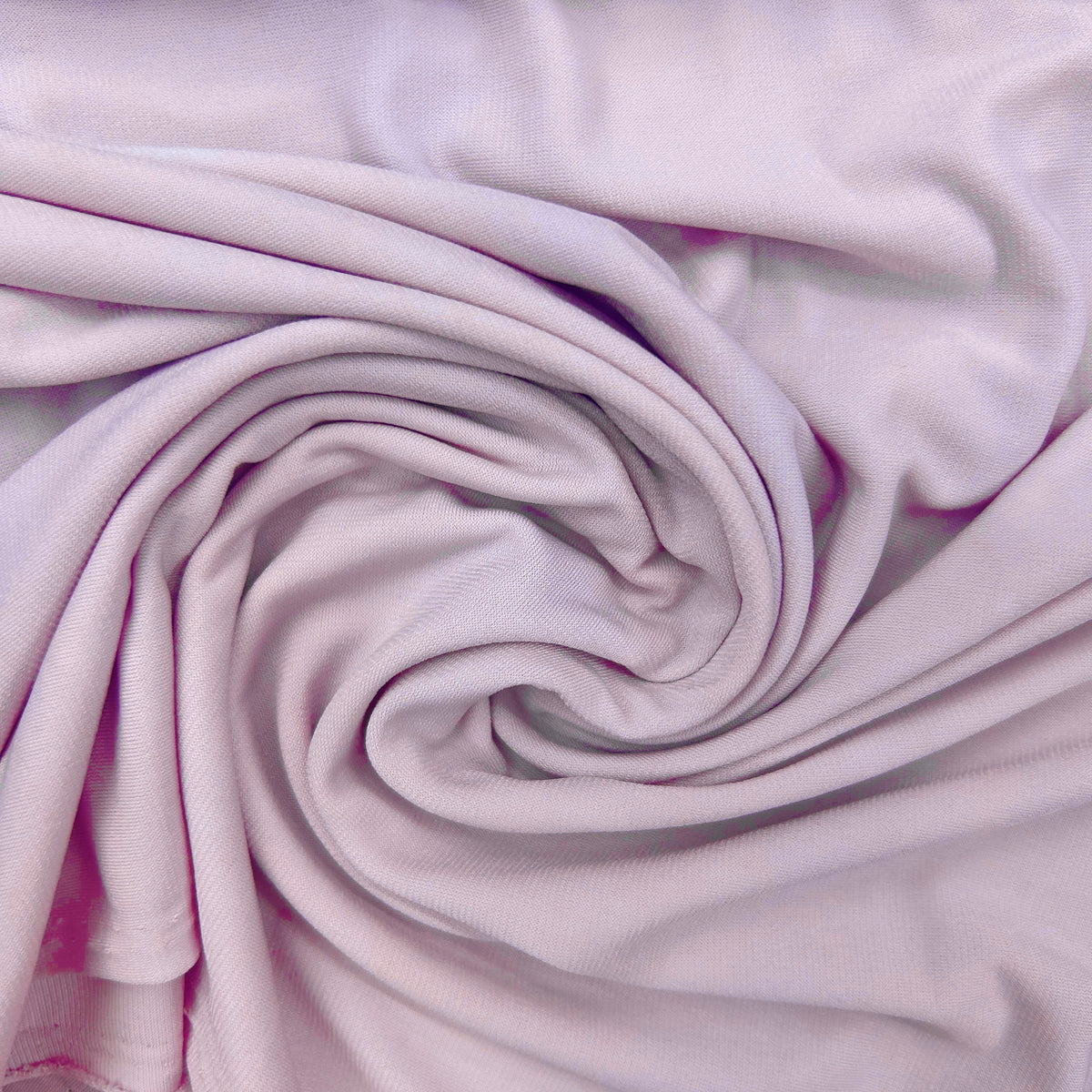 A close-up of light pink fabric arranged in a spiral drape, showing the material texture and soft folds.