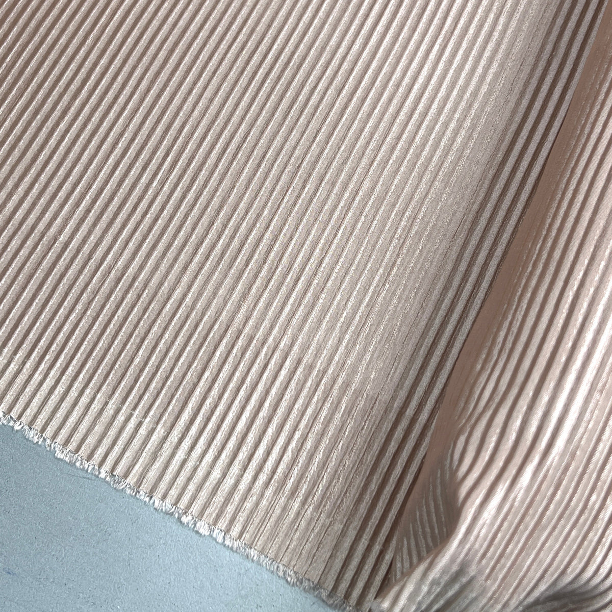 A close-up of a ribbed fabric or material sample in a light warm beige tone, folded to show texture and edge detail.