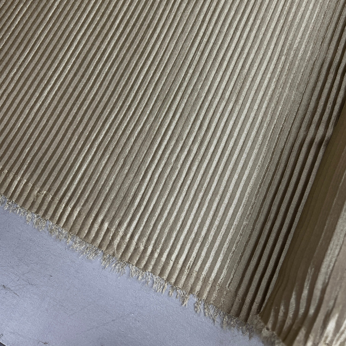 A close-up of a beige ribbed fabric with a frayed edge, laid diagonally across a light gray surface.