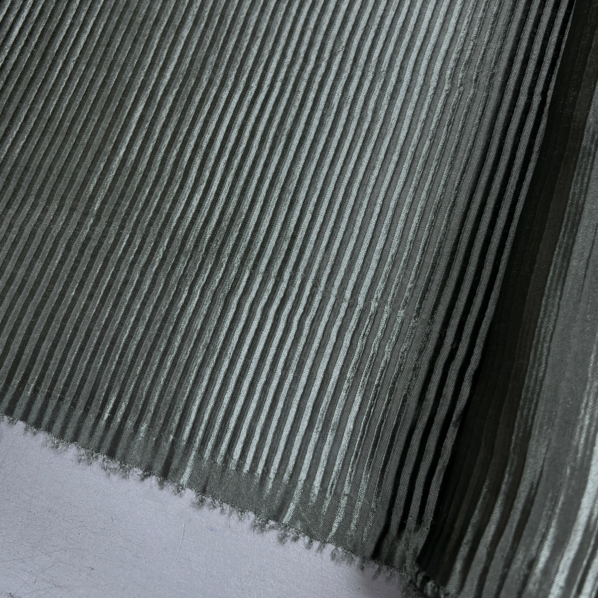 A close-up of a ribbed gray material, likely a textured fabric, wallpaper, or adhesive vinyl sheet, with a white surface visible in the bottom-left corner.