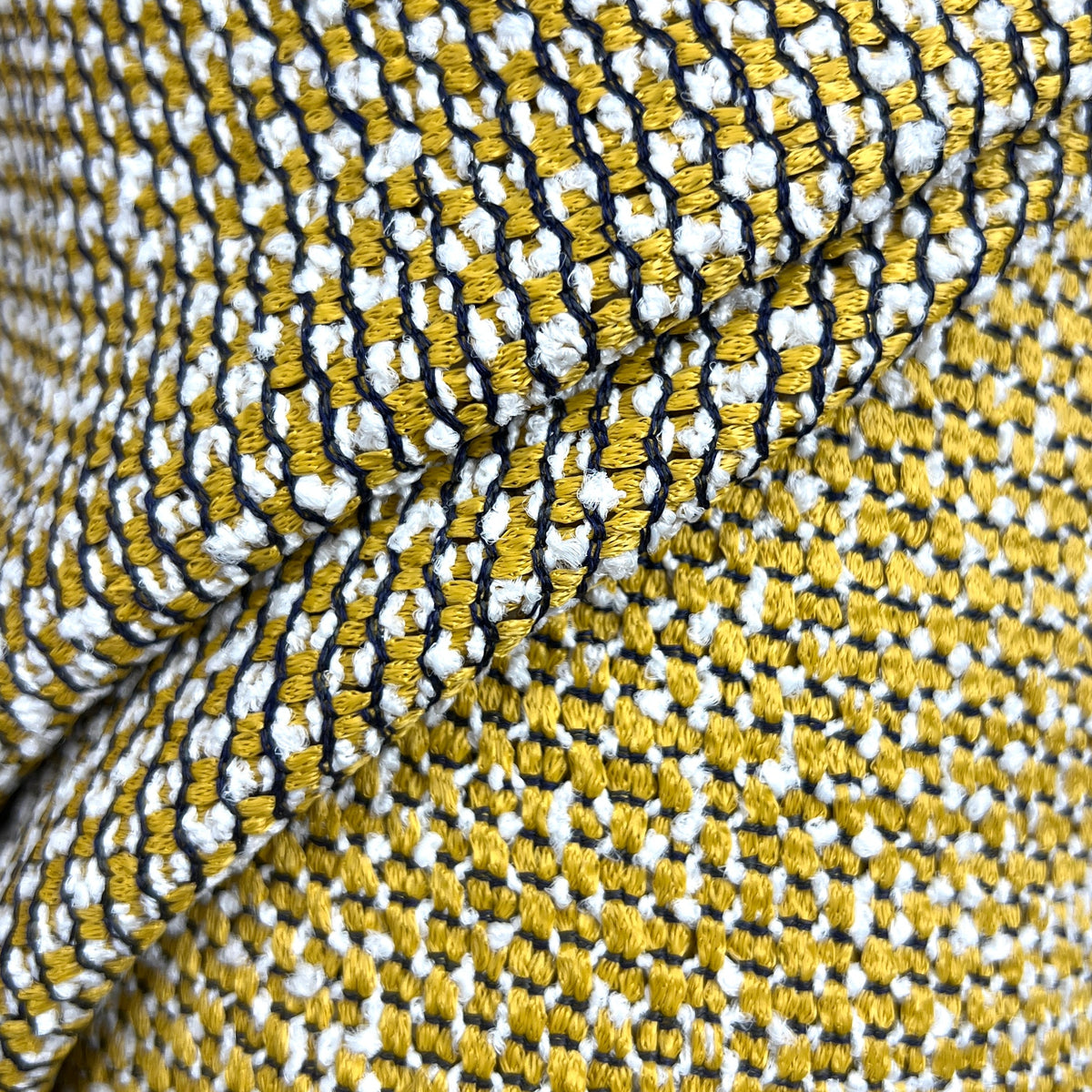A close-up of a textured woven fabric with a repeating pattern of yellow, white, and black threads, draped to show its texture and color composition.