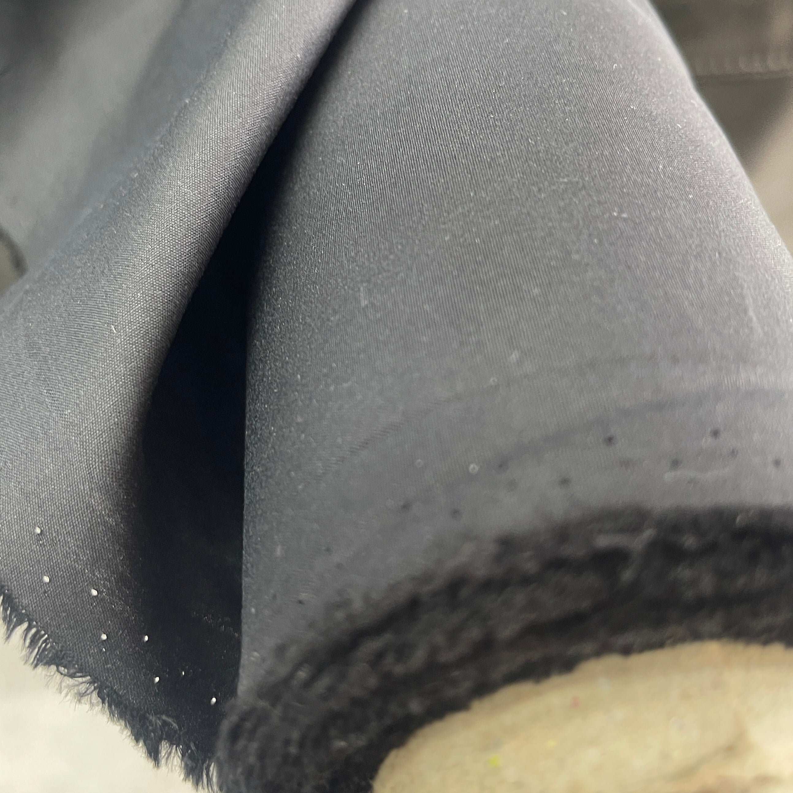 A close-up of a dark charcoal gray fabric roll draped over a light-colored wooden spool, showing the texture and raw cut edge of the material.