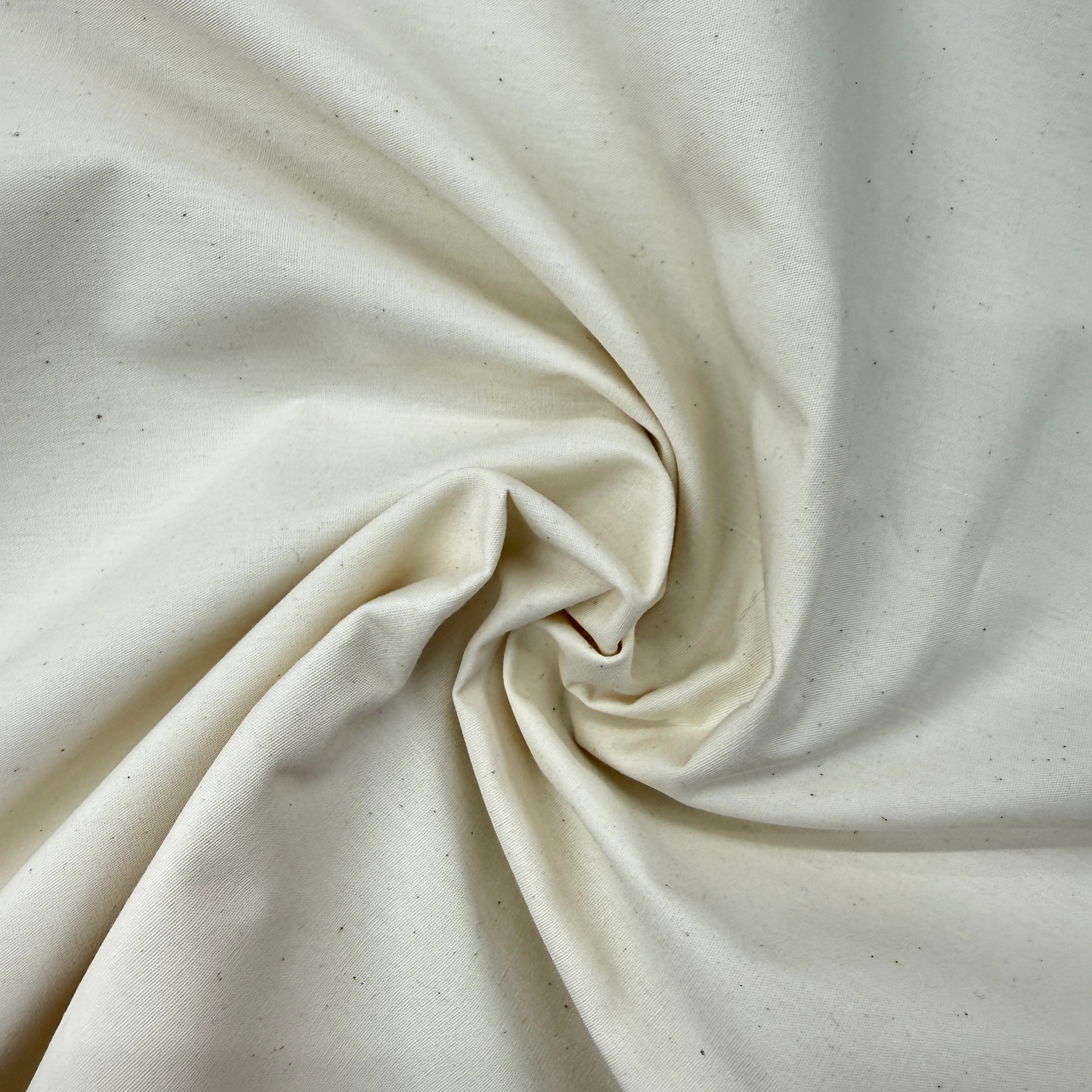 A close-up of off-white fabric with subtle brown speckles, arranged in a spiral drape to show texture and color.