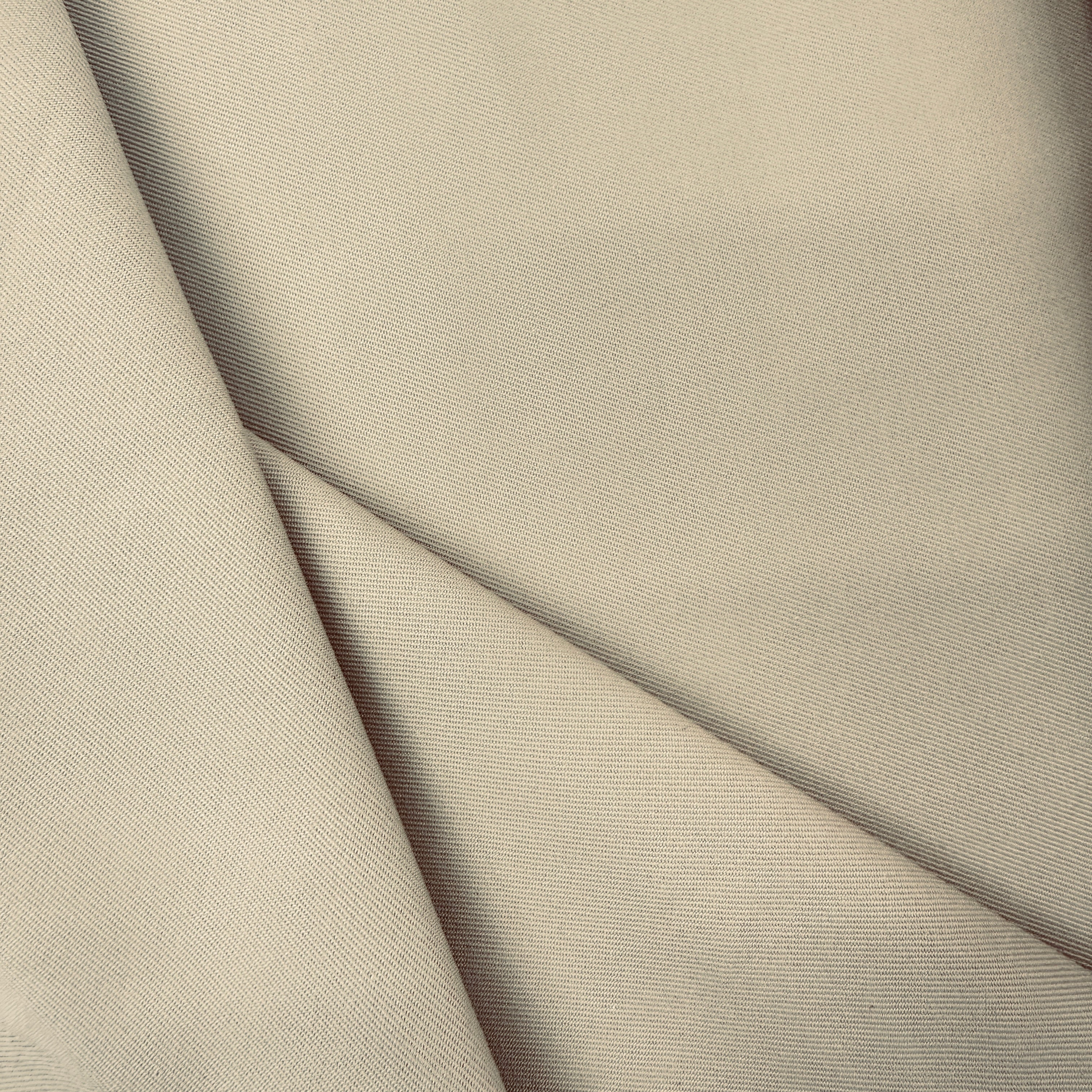 A close-up of draped fabric in a light warm gray or greige color, showing a fine twill texture and soft folds.