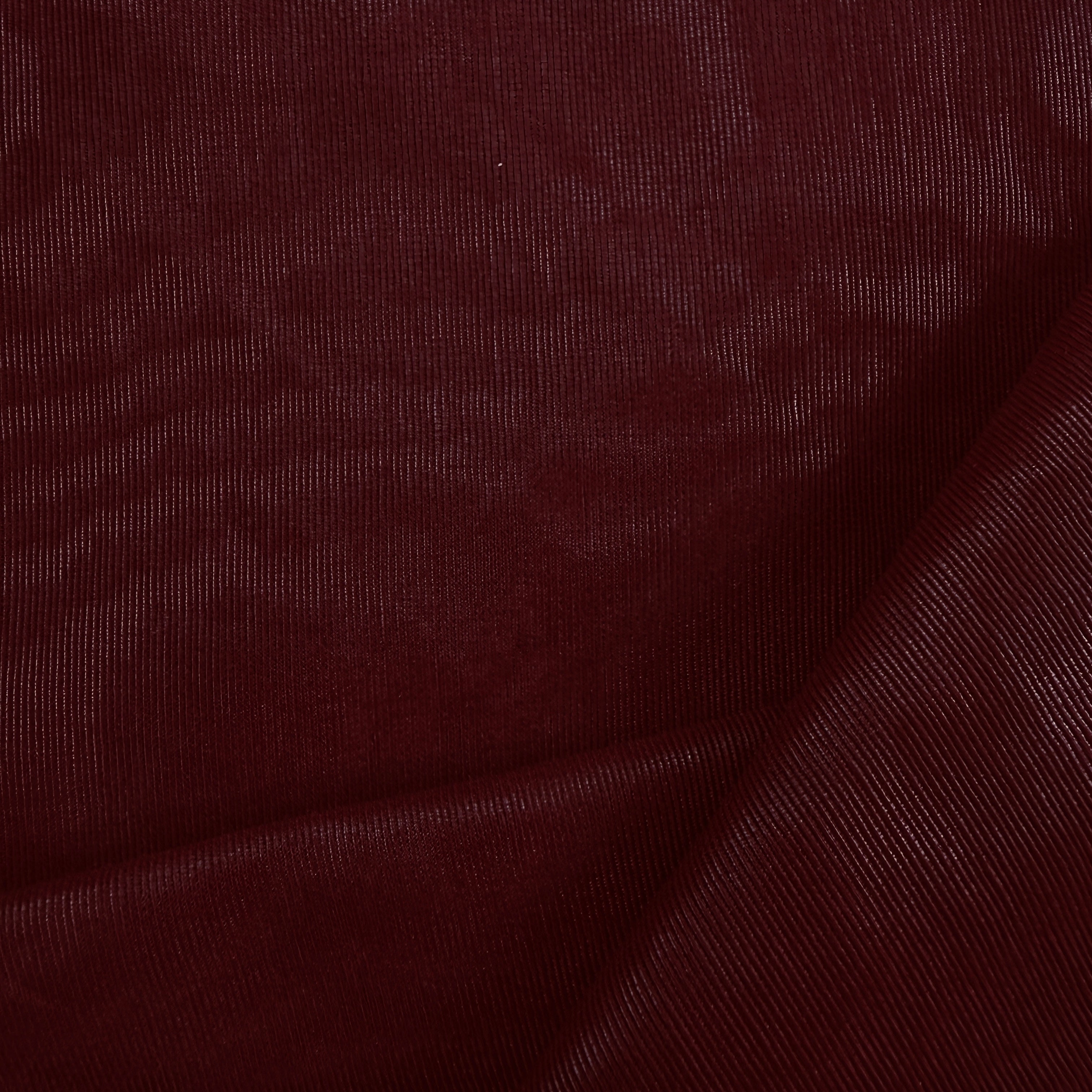 A close-up of dark burgundy fabric with a fine ribbed texture and soft folds.