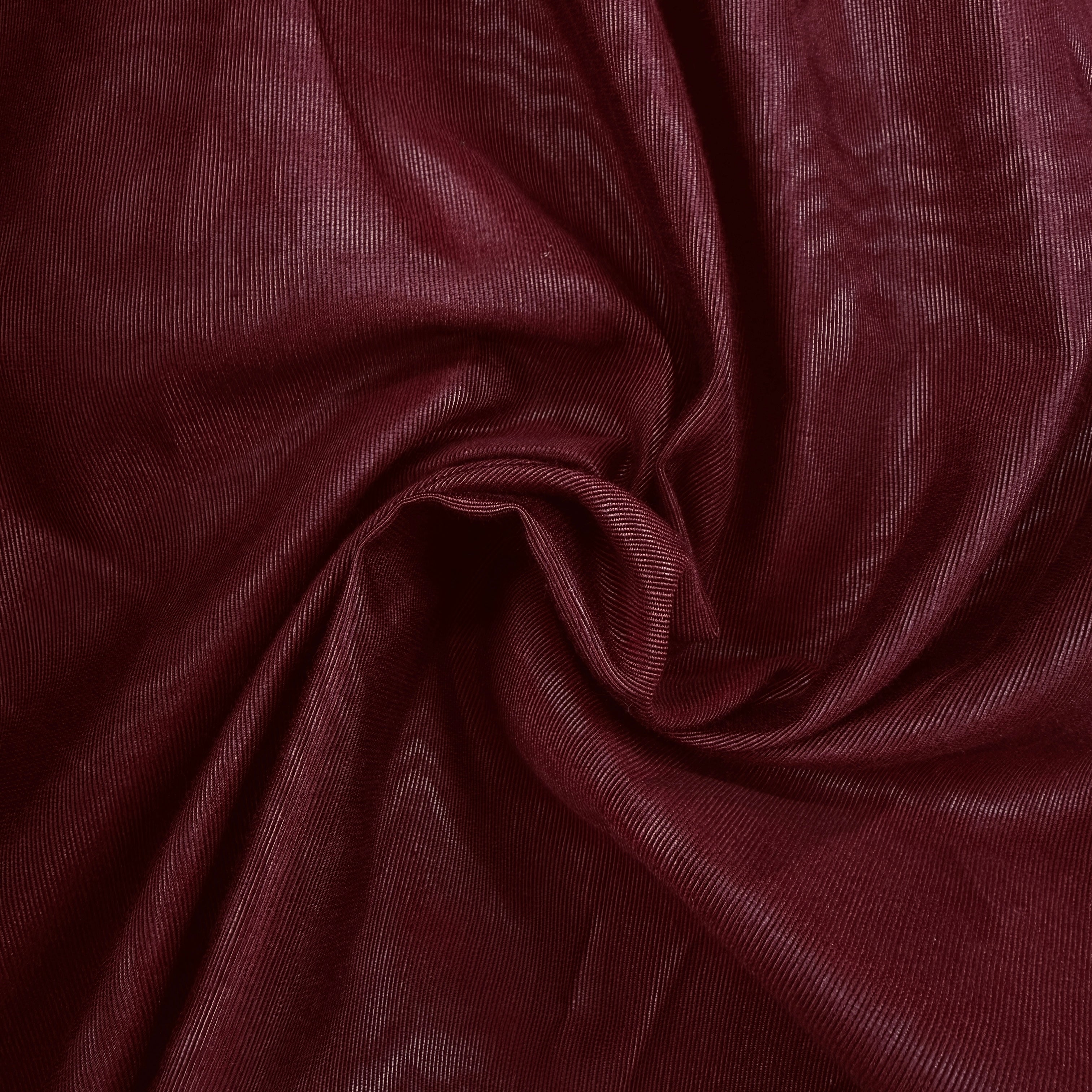 A close-up of draped burgundy fabric with a subtle woven texture, arranged in a central swirl to show the material's drape and sheen.