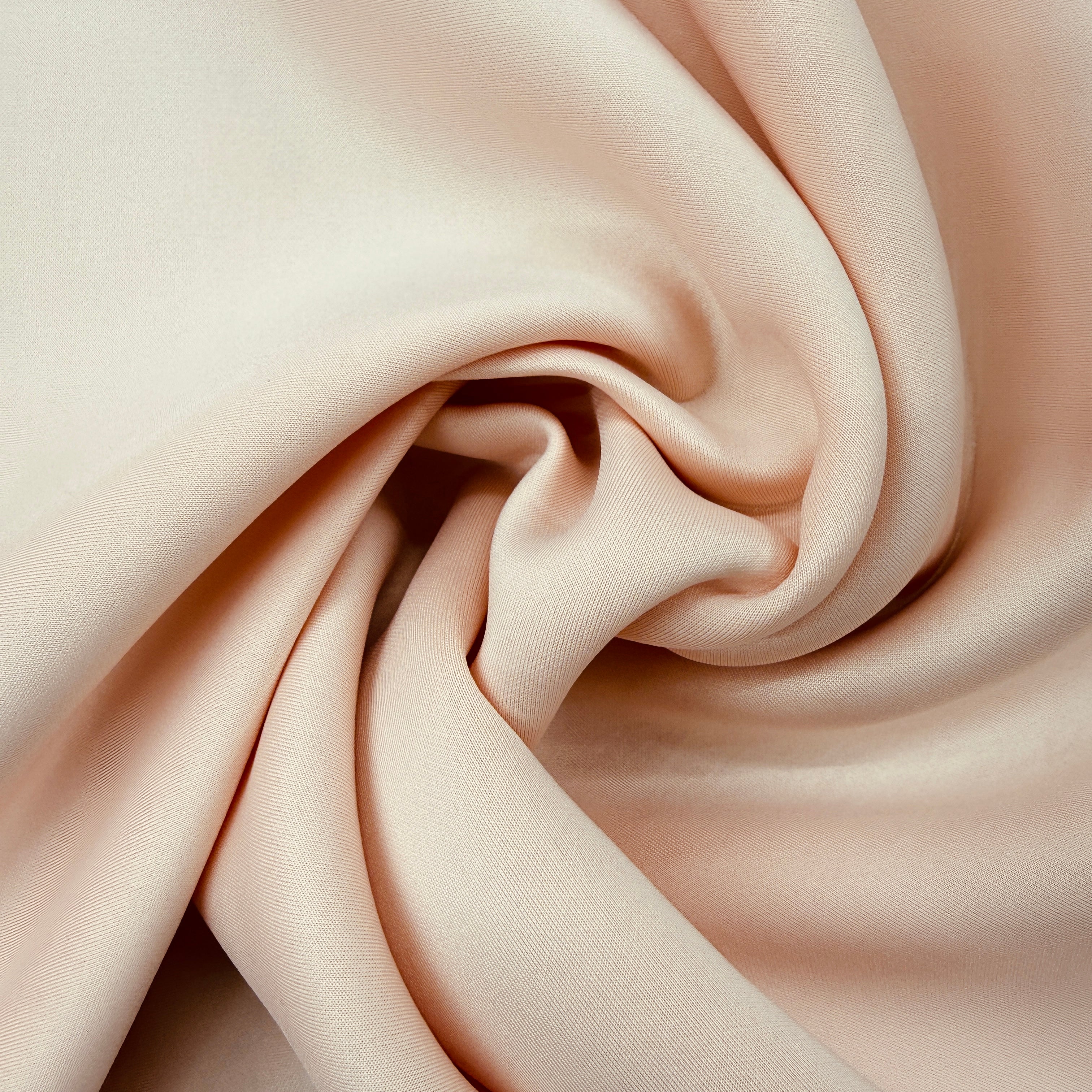 A close-up of draped satin fabric in a soft blush pink color, arranged in a central swirl to show its smooth texture and sheen.