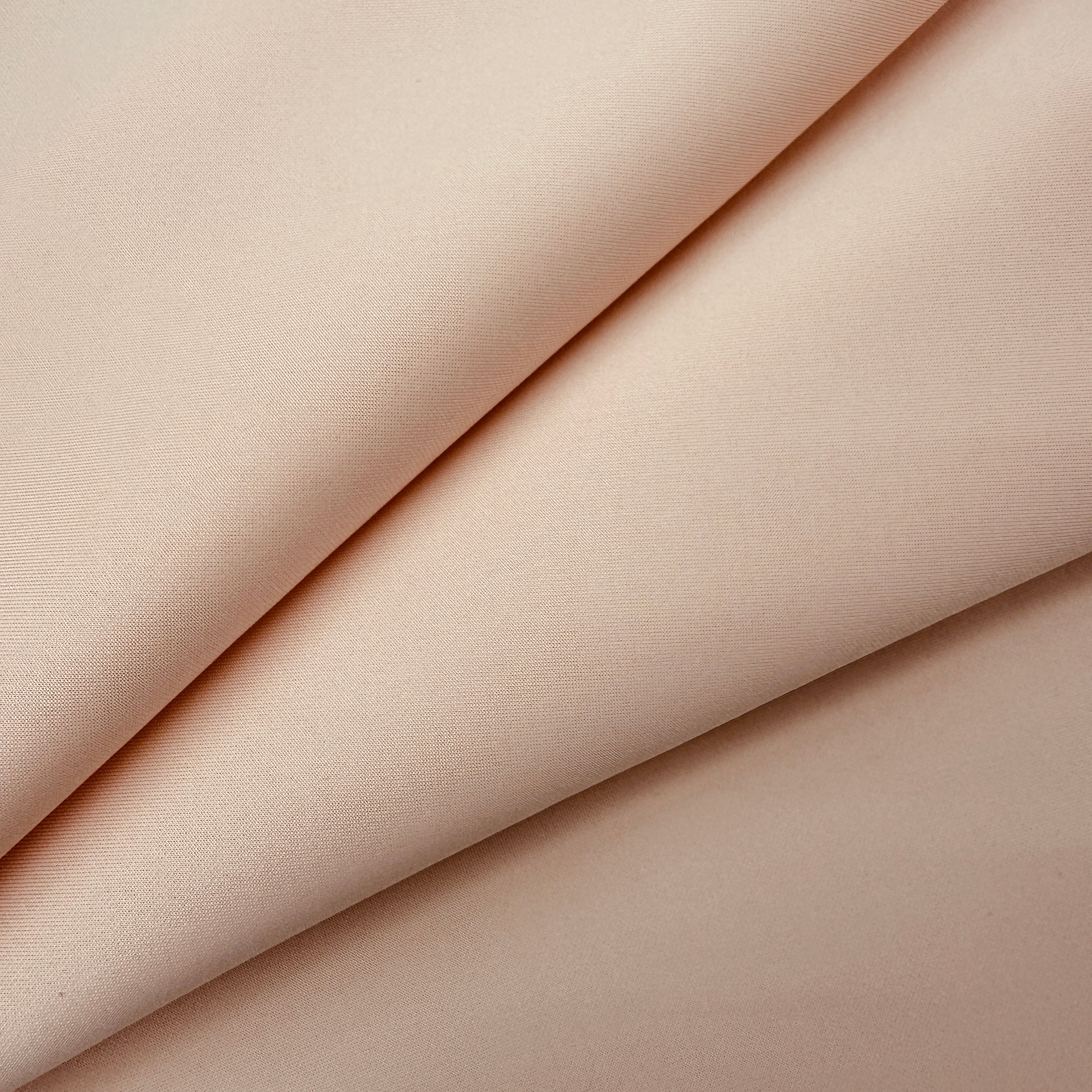 A close-up of draped fabric in a soft warm blush or nude tone, showing the material texture and folds.