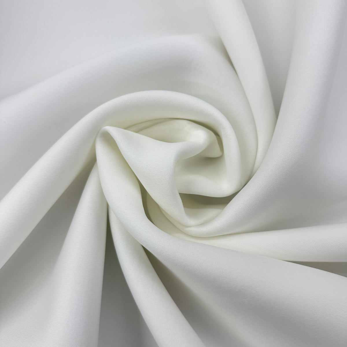 A close-up of white satin or silk fabric arranged in a spiral drape, showing its smooth texture and soft sheen.