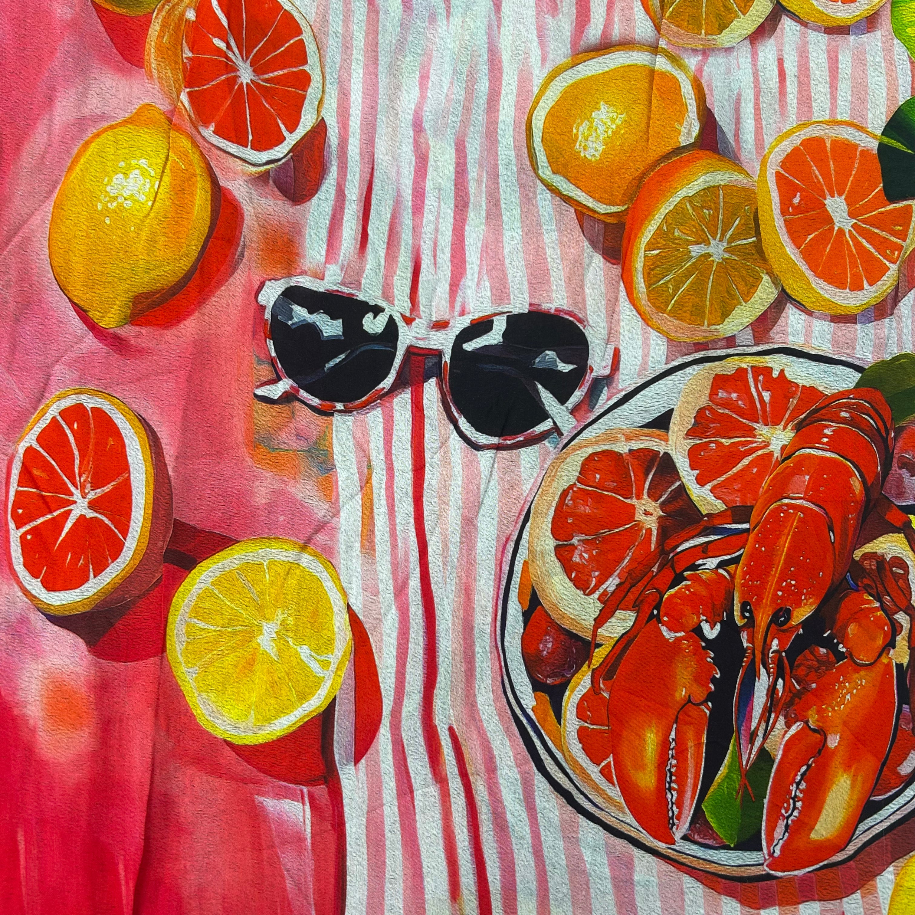 Colorful towel with lemons, oranges, a bowl of lobsters, and sunglasses on a pink and white striped background.