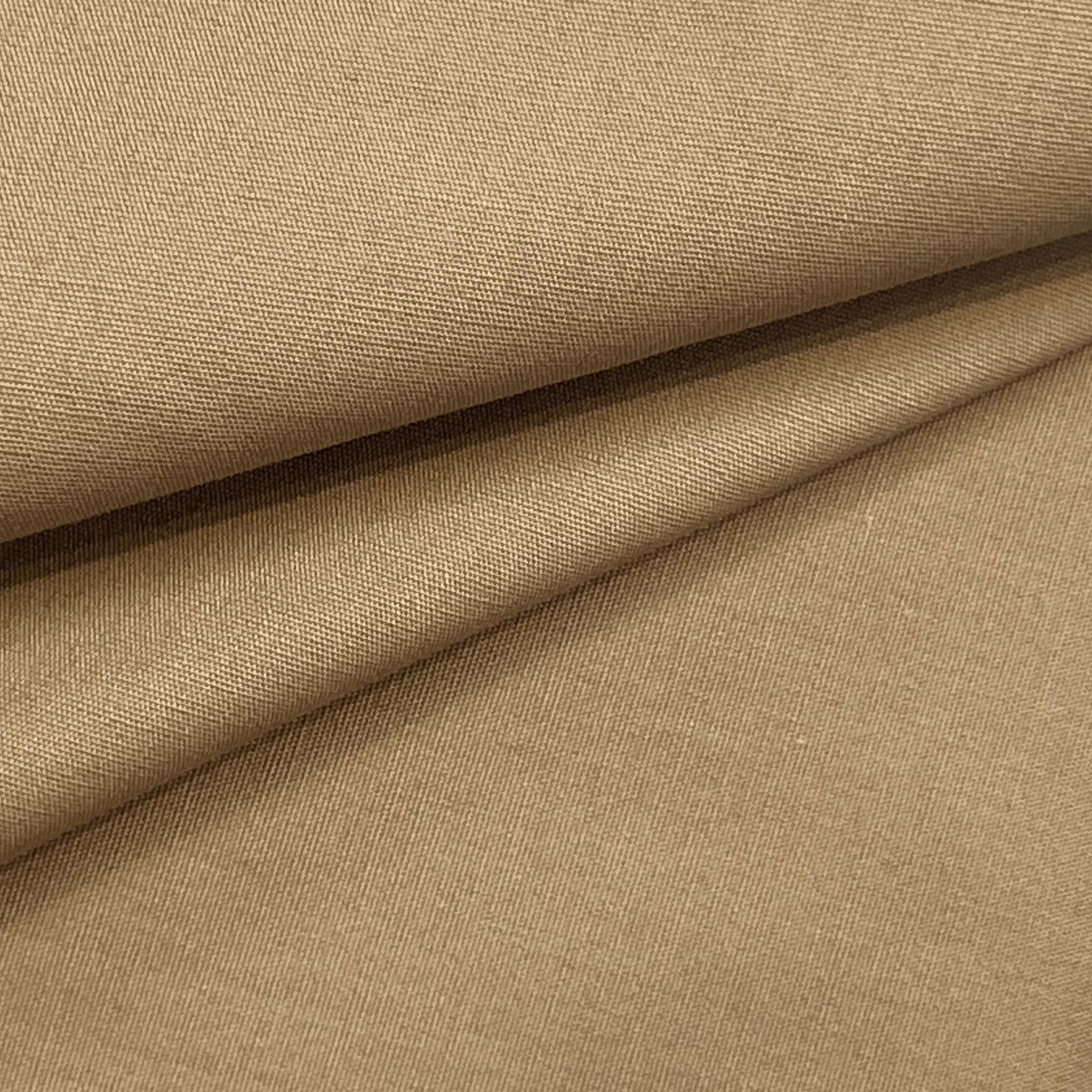 Close-up of folded tan cotton poplin fabric showing its fine, smooth plain weave texture.