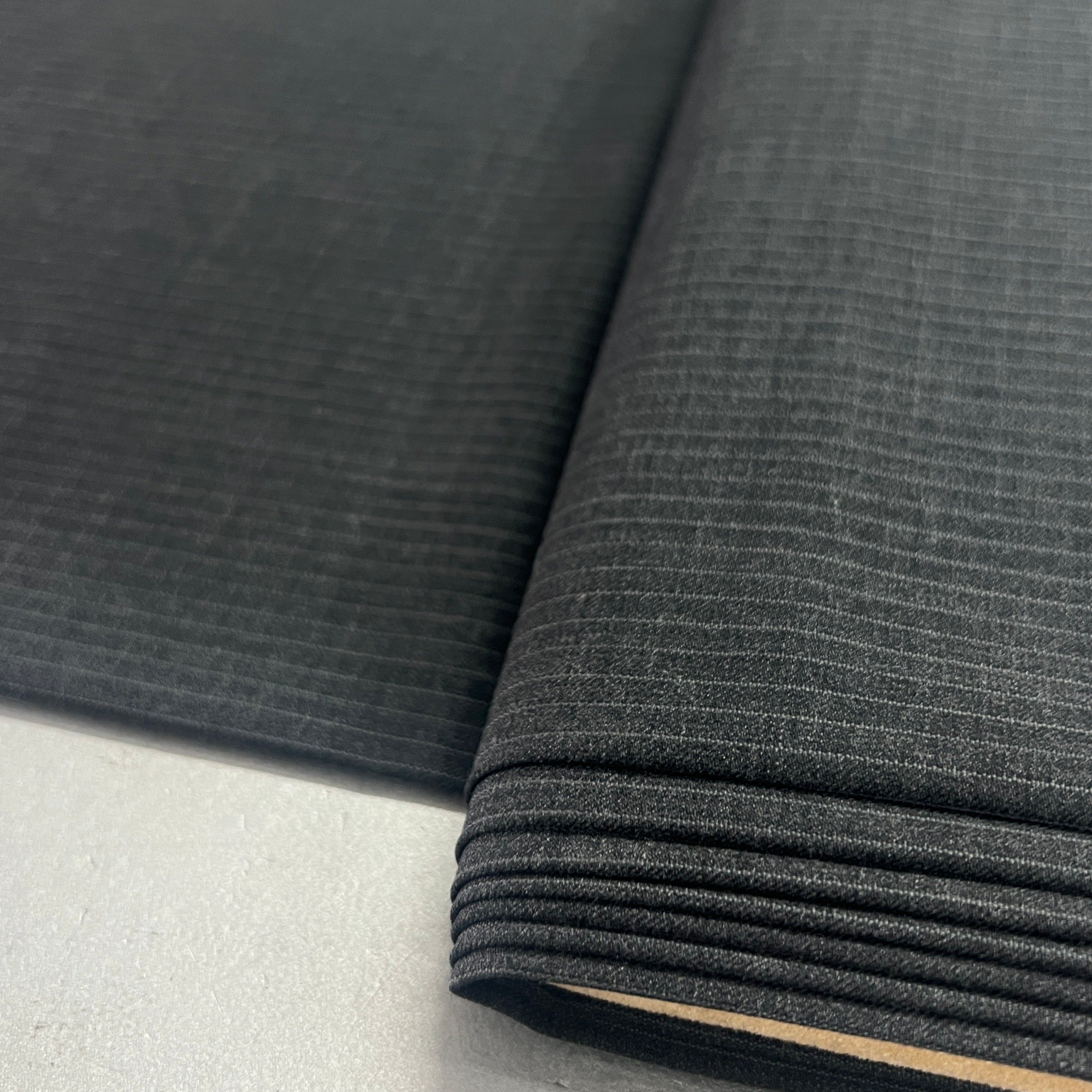 A close-up of dark charcoal gray ribbed fabric, folded over to show its texture and layered edges, resting on a light gray surface.