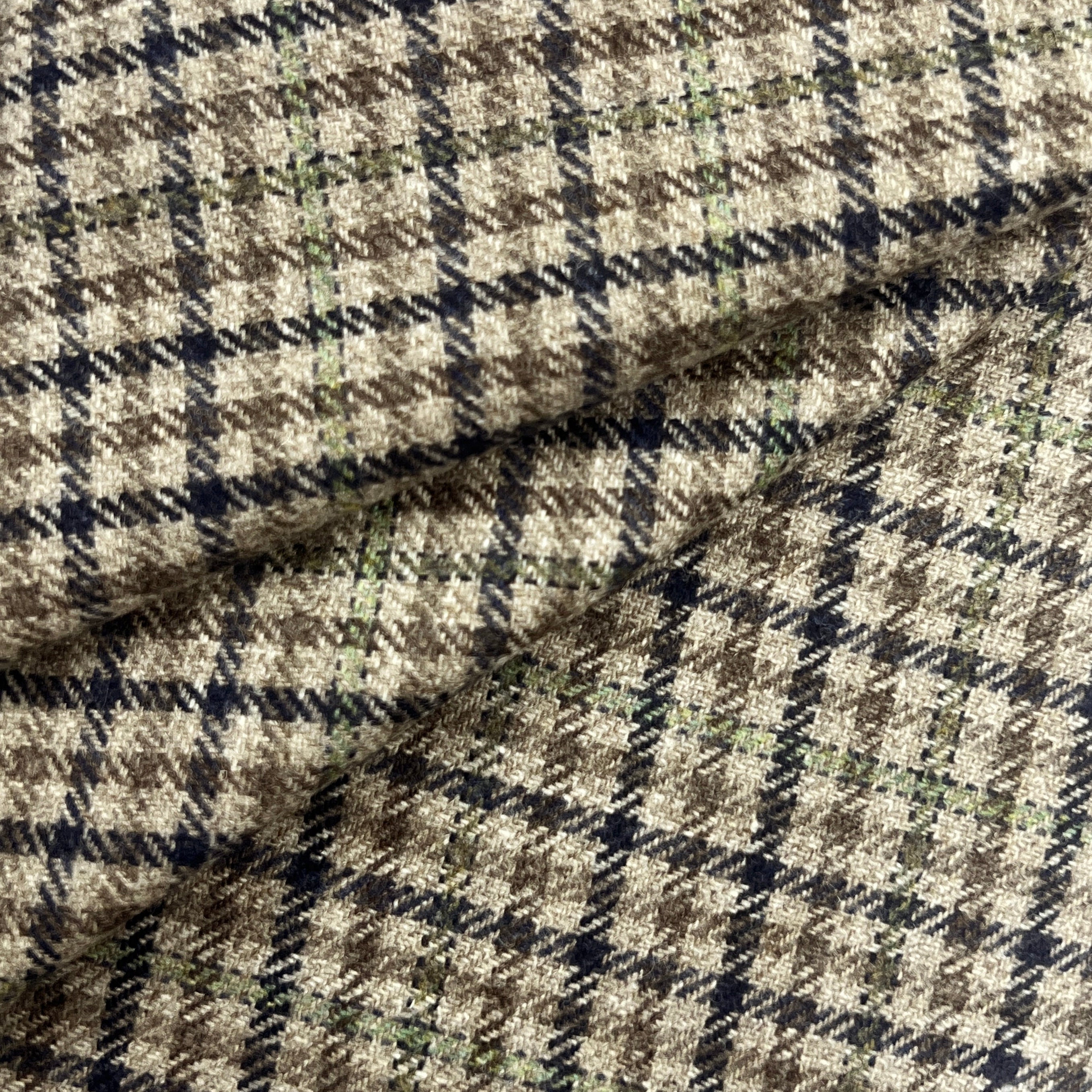 A close-up of a textured woven fabric with a classic plaid pattern in beige, brown, black, and subtle light green stripes.