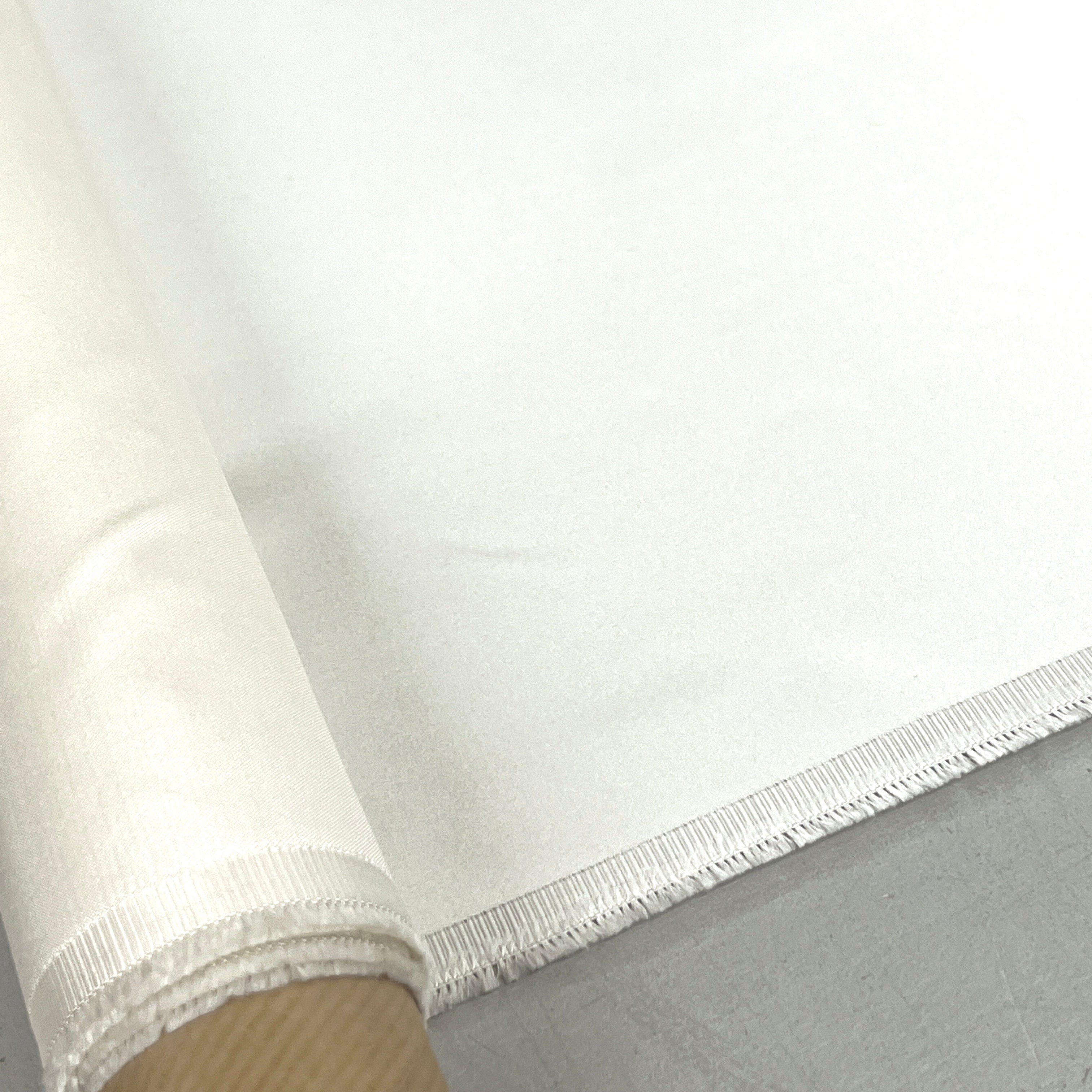A close-up of a white fabric roll with a frayed edge, partially unrolled over a neutral gray surface.
