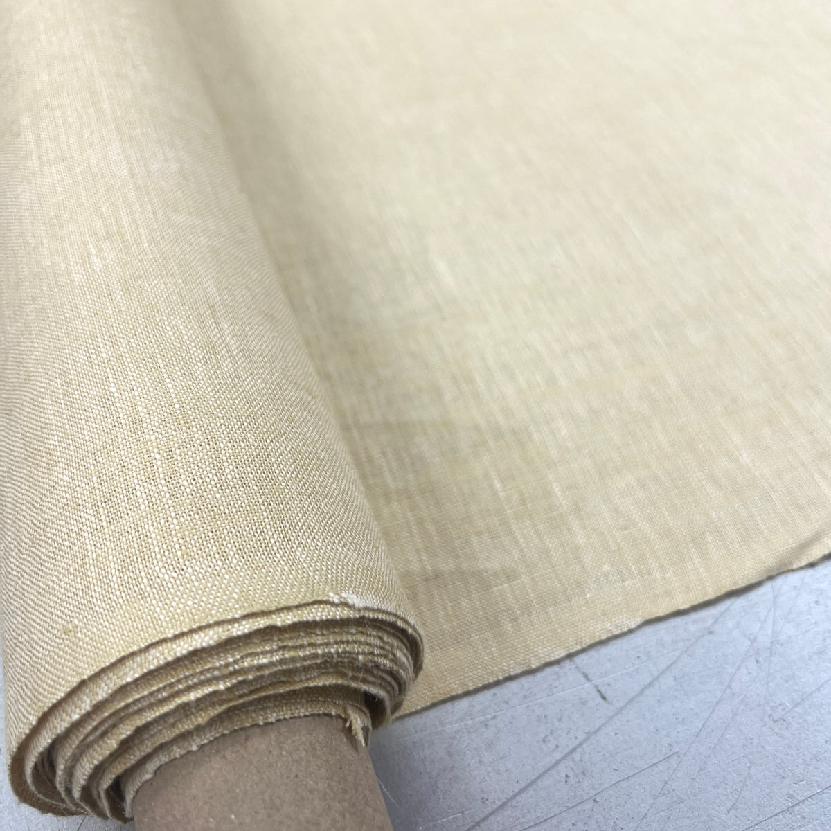 A close-up of a roll of light beige woven fabric or canvas material unrolled over a gray surface.
