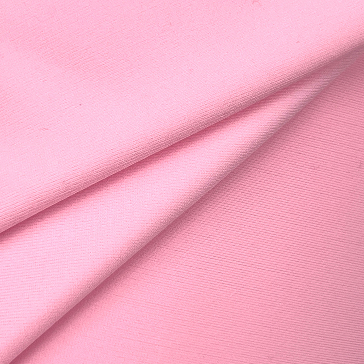 A close-up of light pink fabric with a fine ribbed texture, folded diagonally across the frame.