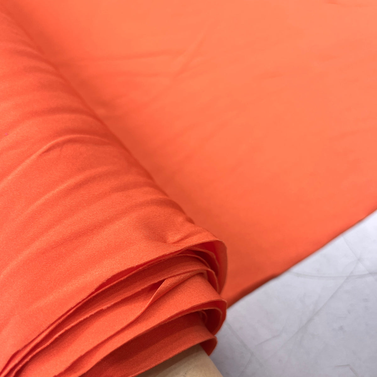 Bright orange fabric draped over a cardboard roll, showing a smooth texture and soft folds.