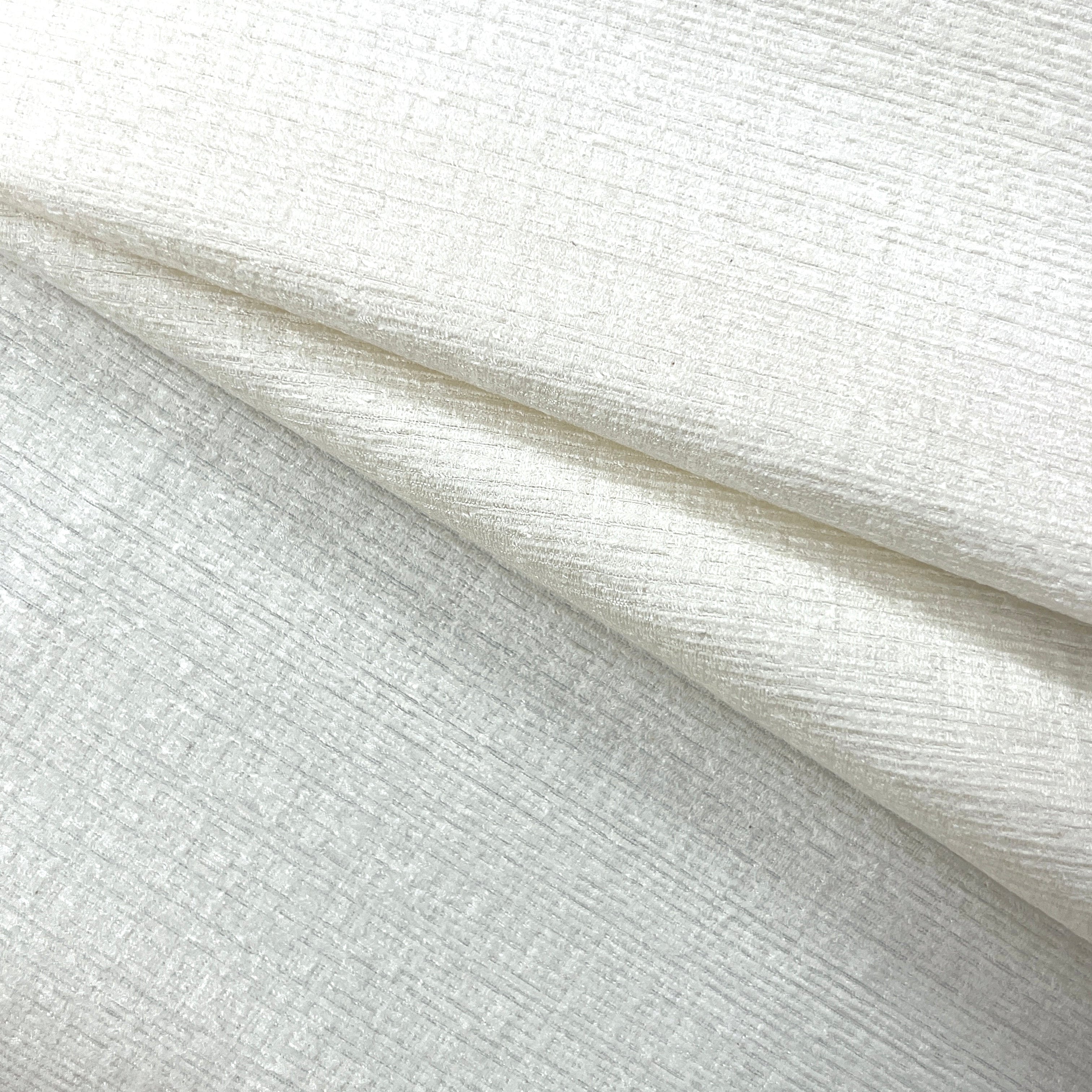 A close-up of textured off-white fabric with a subtle linen-like weave, shown folded to highlight its soft drape and surface detail.