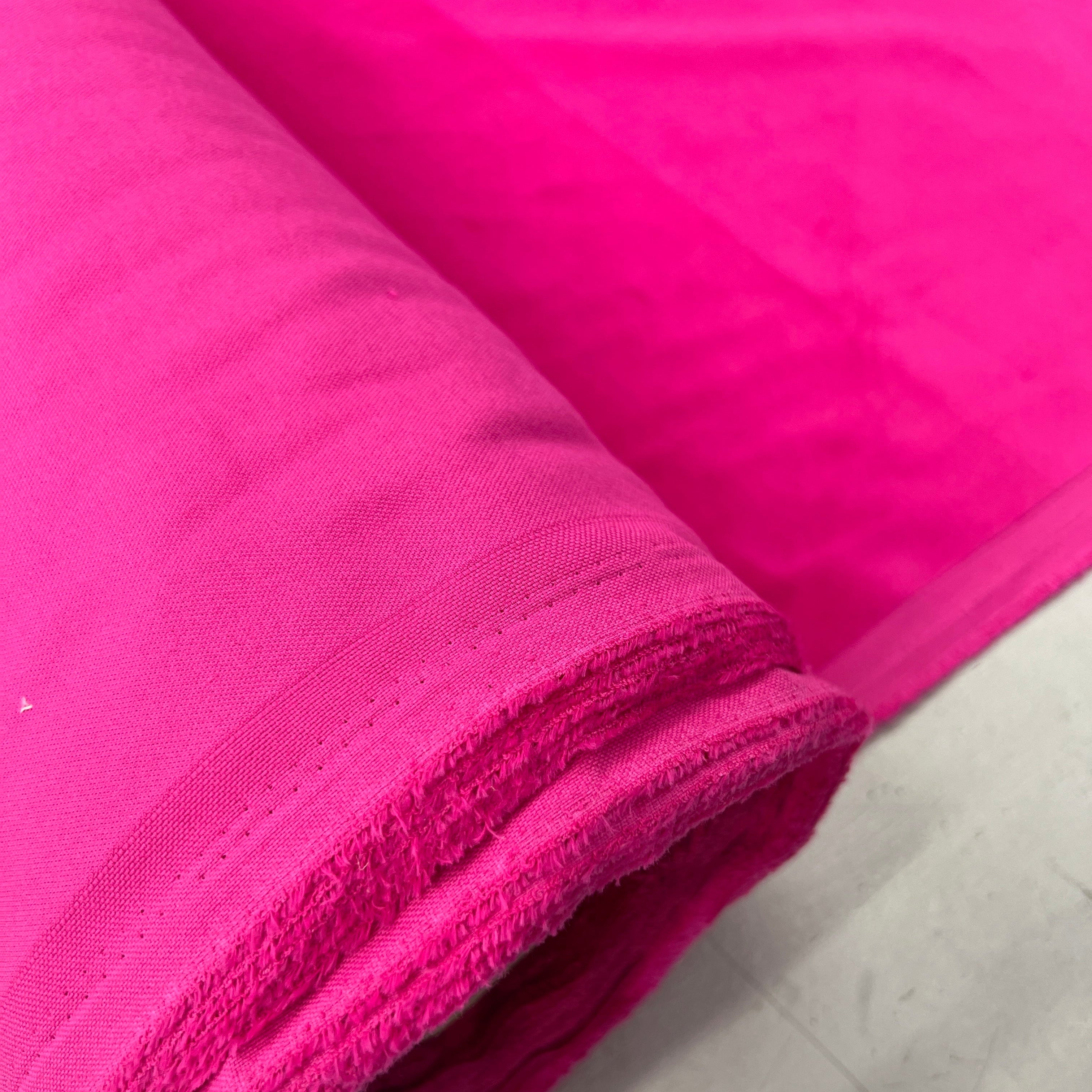 A close-up of a bright hot pink fabric, shown rolled over to display its texture and weave, resting on a light gray surface.