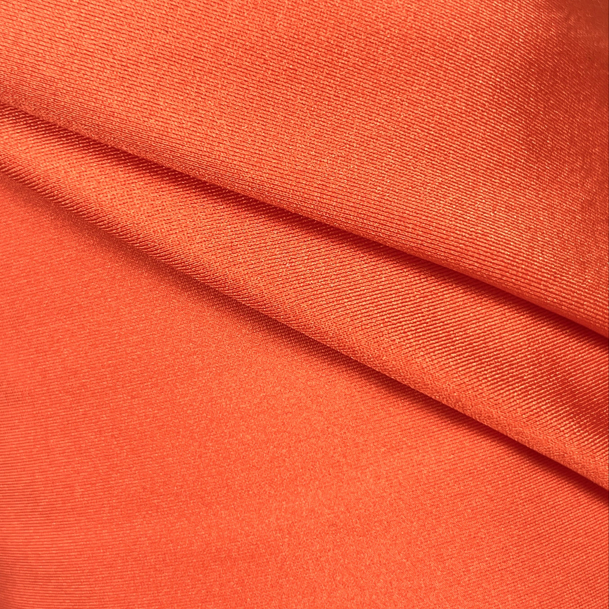A close-up of draped orange fabric with a smooth texture and soft folds.