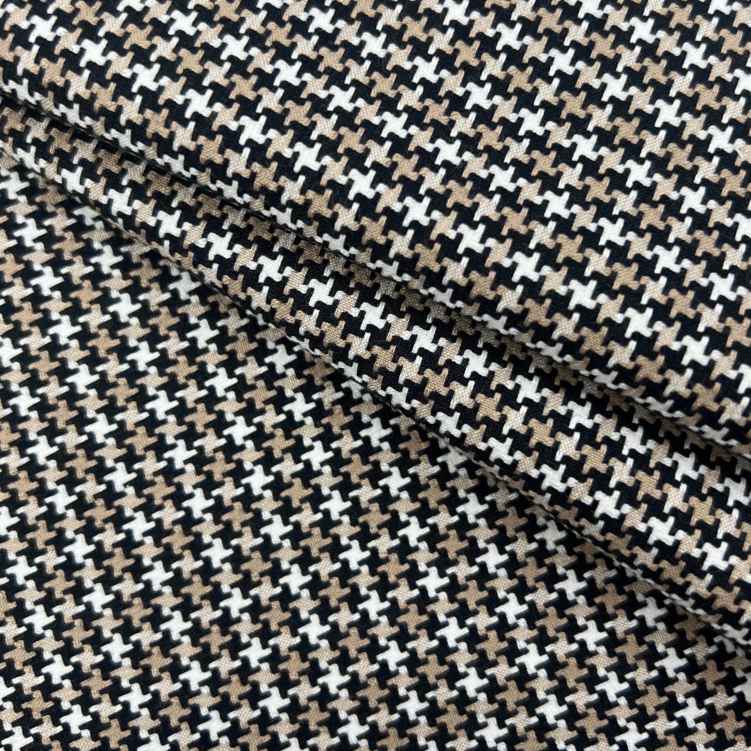 A close-up of a folded fabric with a repeating houndstooth-like pattern in black, beige, and white.