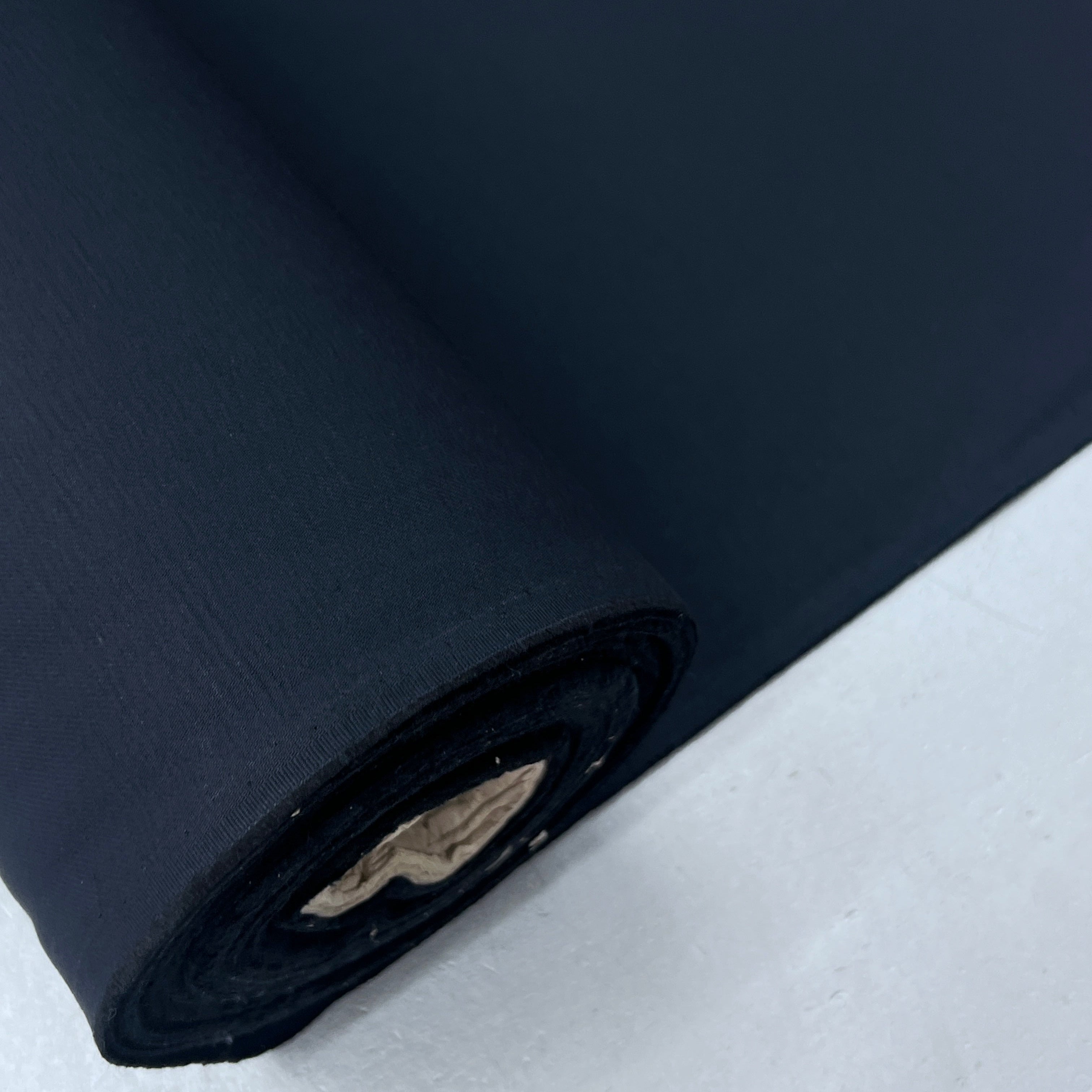 A close-up of a rolled dark navy fabric or material on a light gray surface.