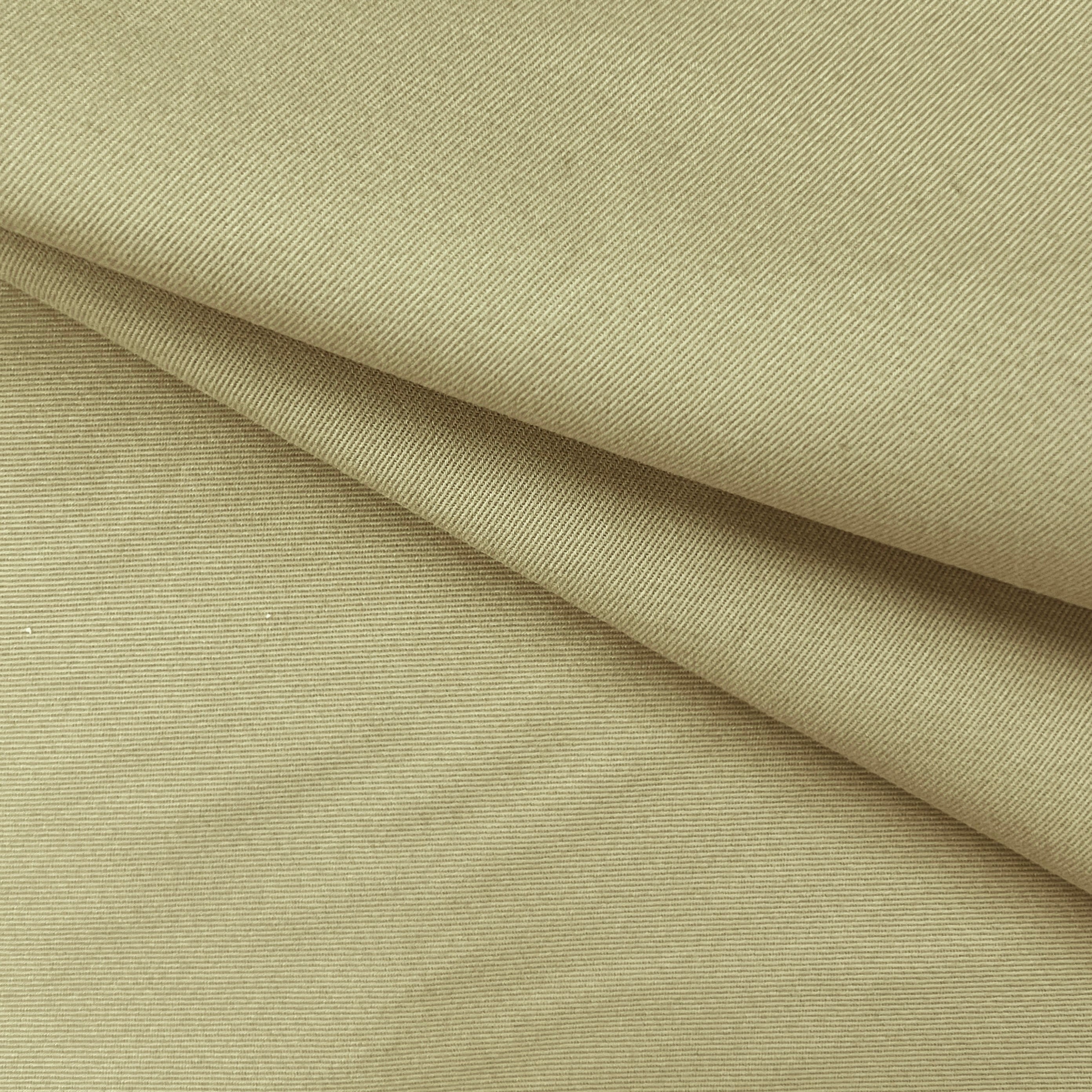 A close-up of draped beige fabric with a fine twill texture and soft folds.