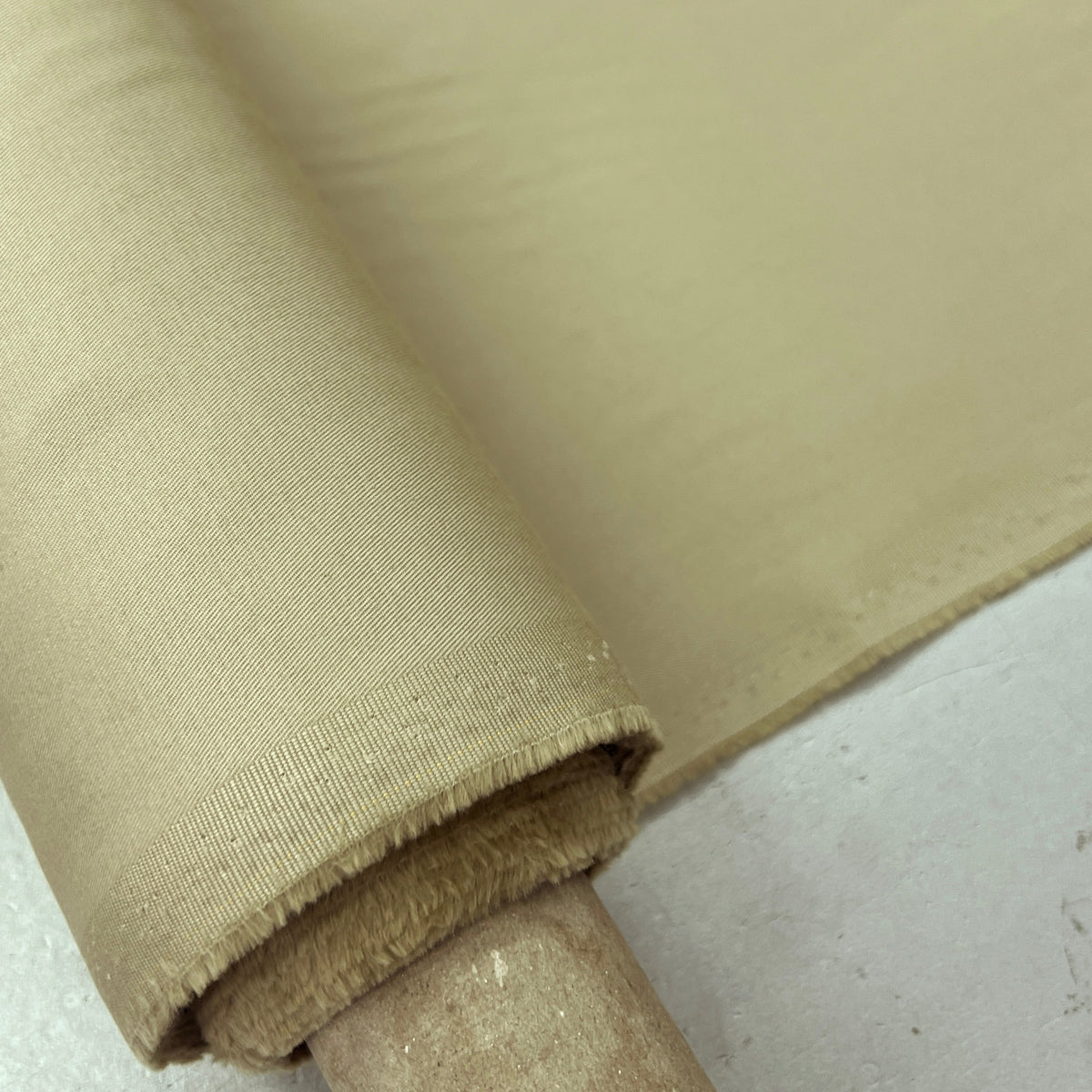 A close-up of a roll of beige fabric draped over a wooden spool, showing the woven texture and color of the material.