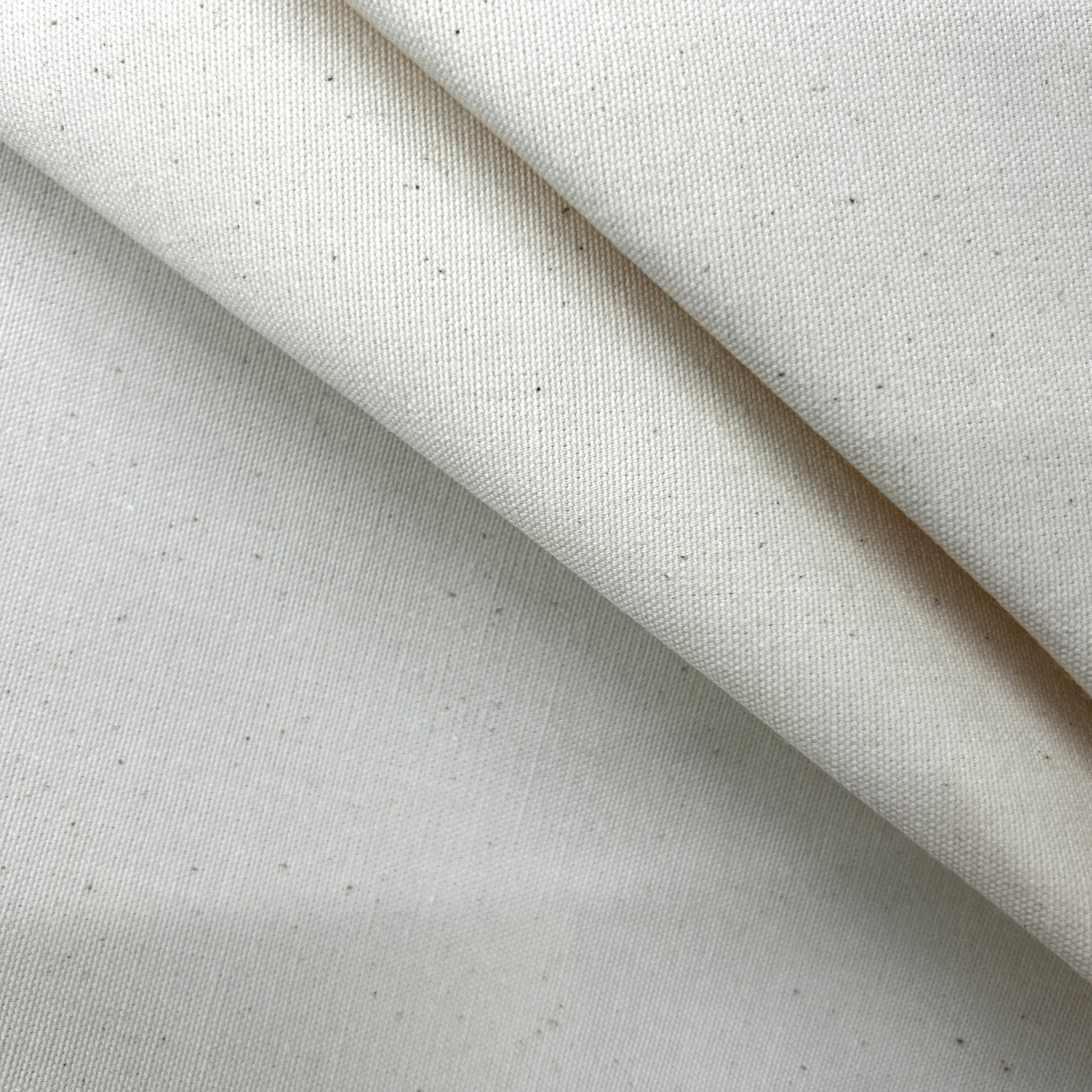A close-up of off-white woven fabric with a subtle speckled texture, folded diagonally to show the material's drape and weave.