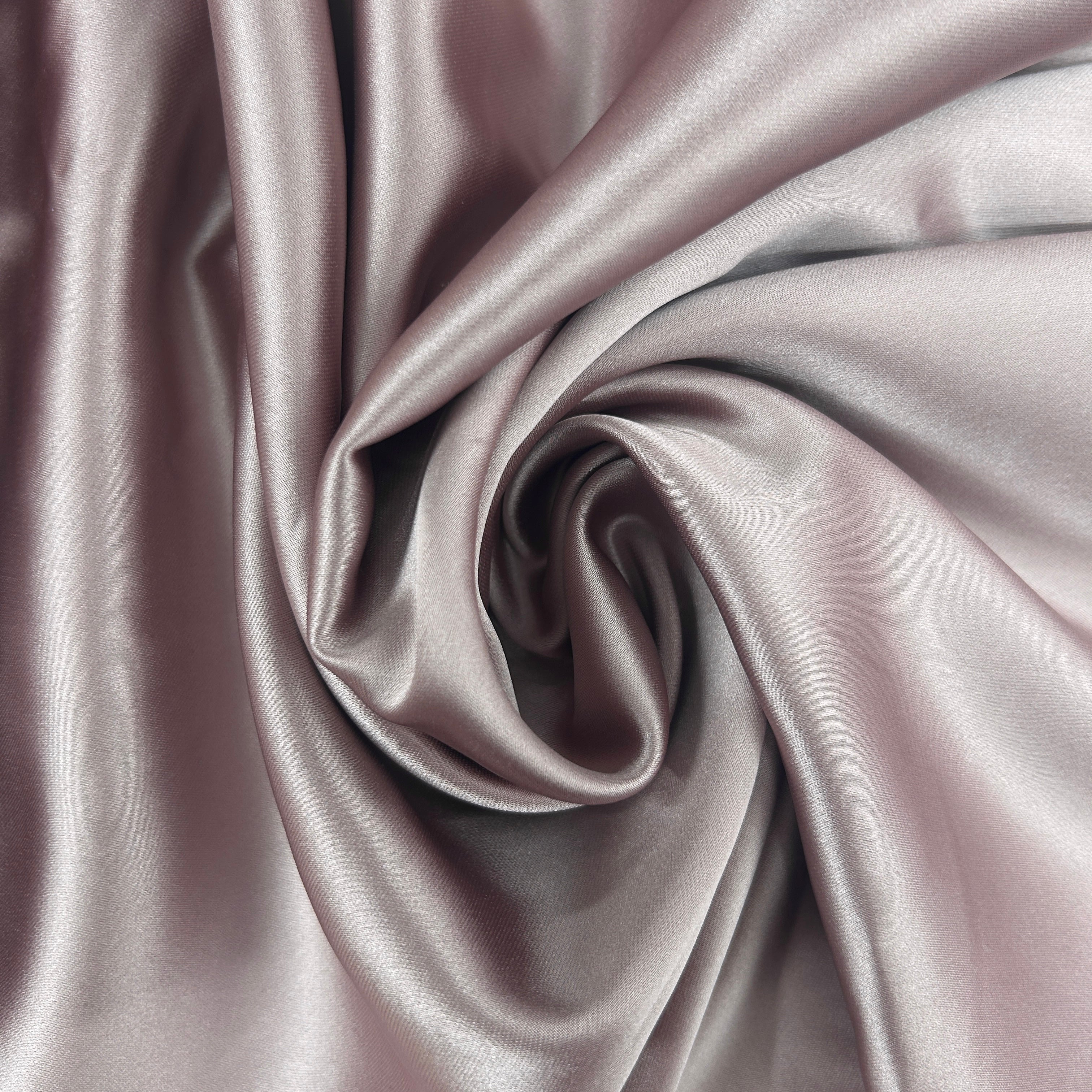 A close-up of draped satin fabric in a dusty lavender-gray color, arranged in a central swirl to show its smooth texture and sheen.