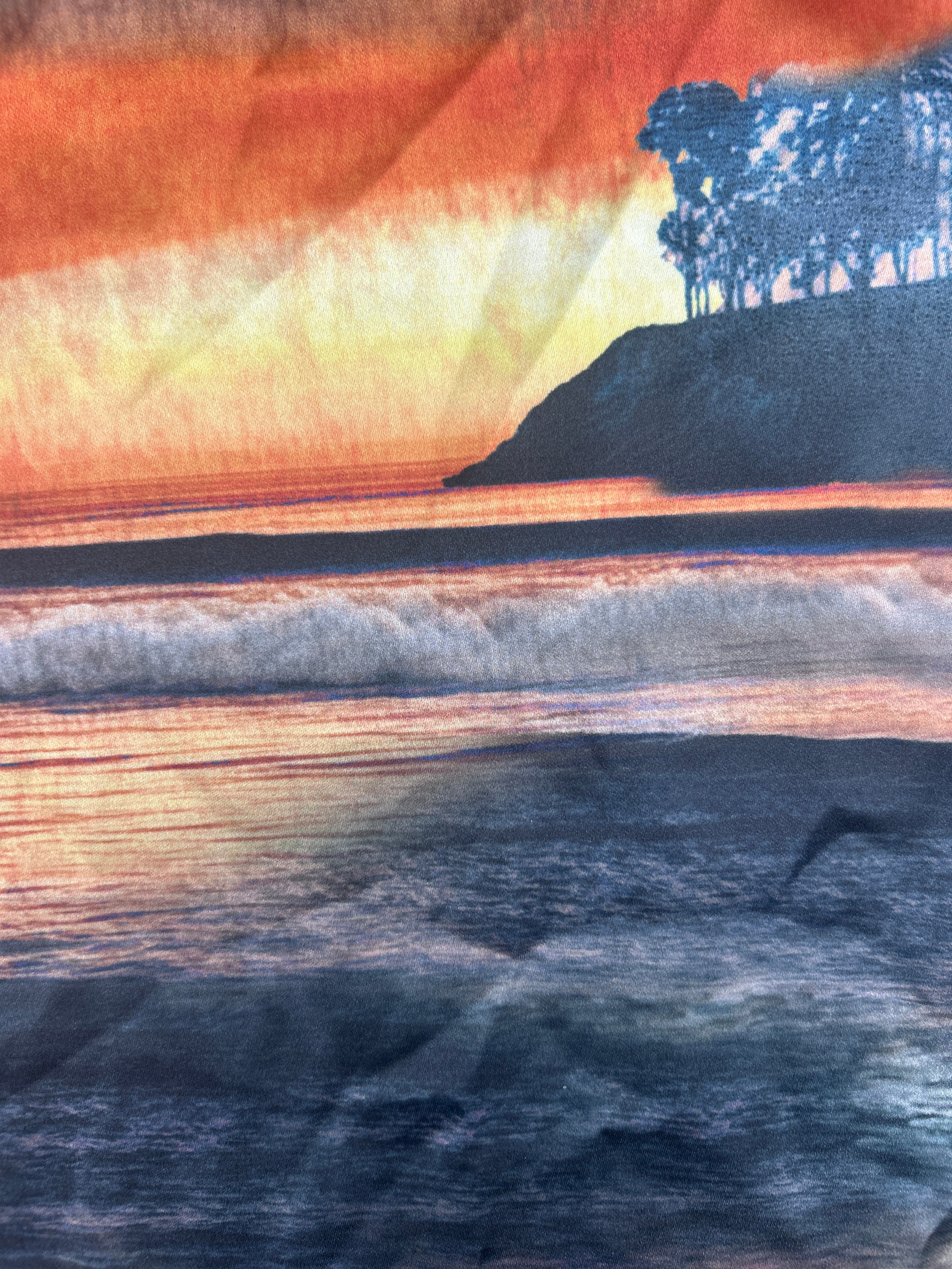 A close-up of a printed fabric or wallpaper pattern depicting a landscape scene with vertical rock formations in shades of orange, yellow, brown, black, and gray.