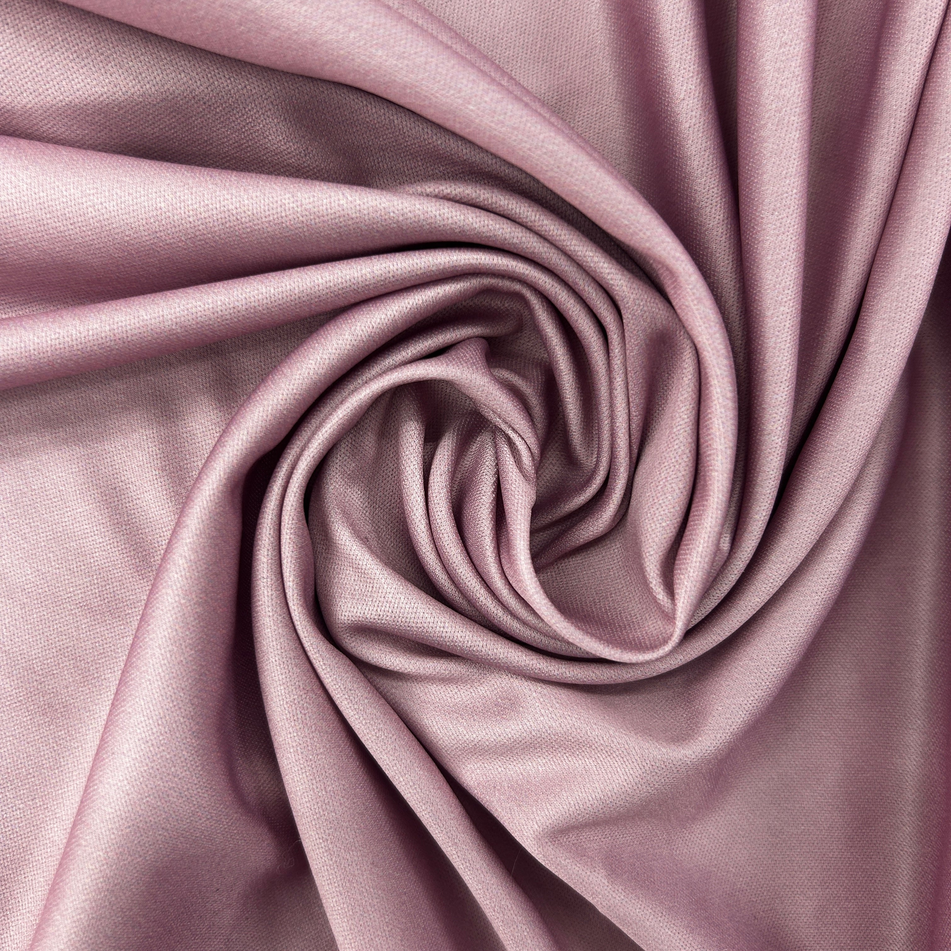 A close-up of draped dusty pink satin fabric arranged in a spiral pattern, showing its smooth texture and sheen.