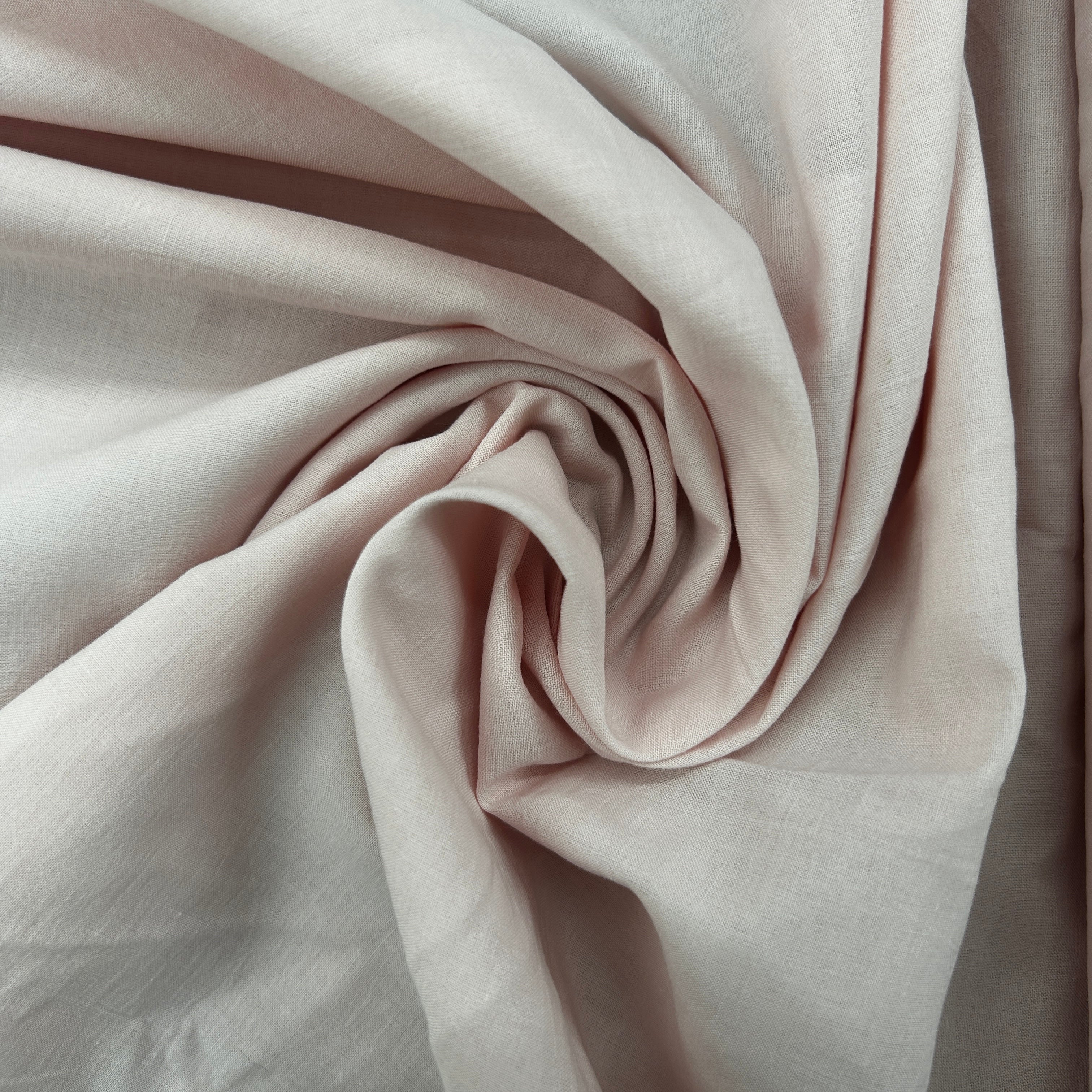 A close-up of draped fabric in a soft blush pink color, arranged in a spiral pattern to show its texture and drape.