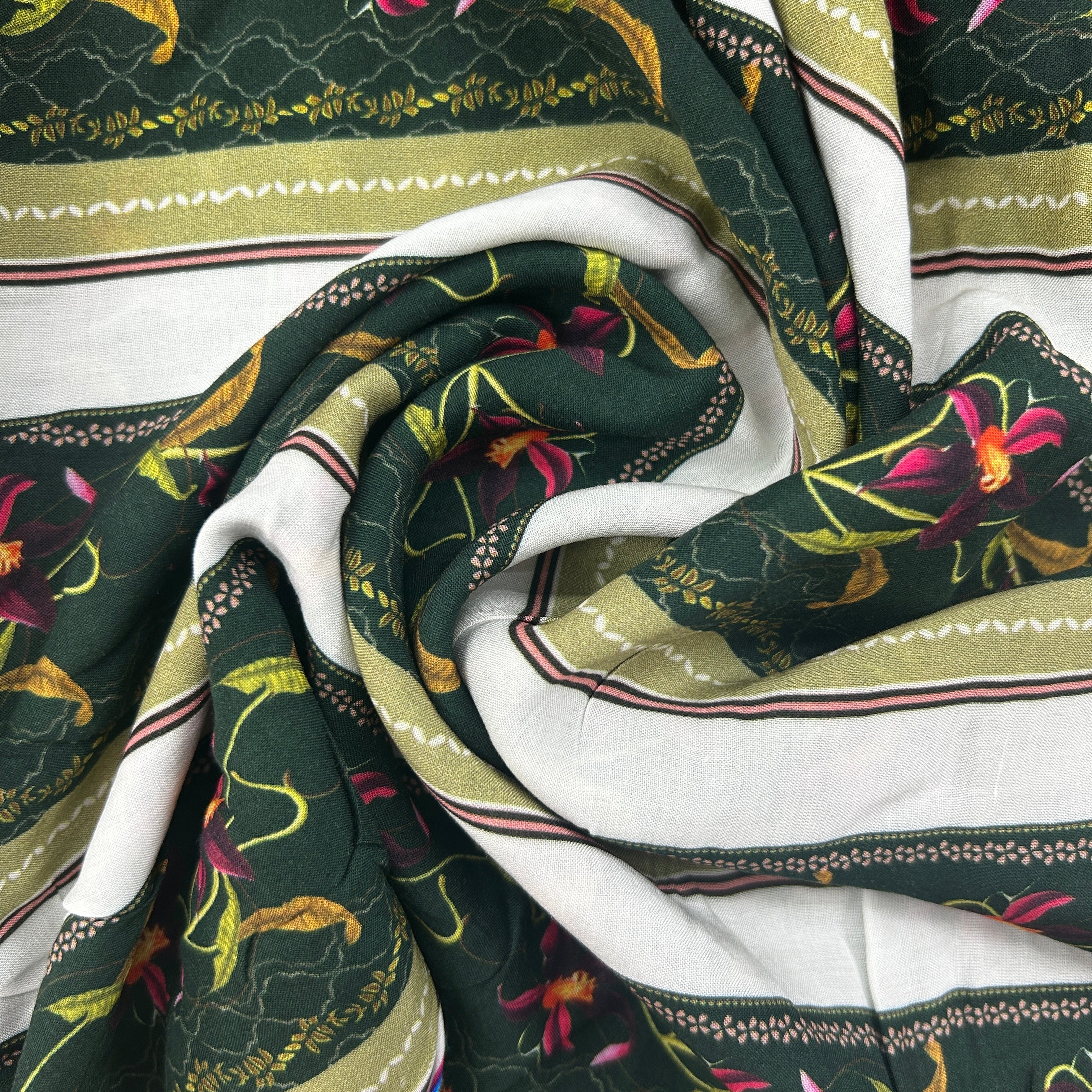 A close-up of a draped fabric with a dark green base, featuring a white border, olive green stripes, and a botanical print with pink and yellow flowers.