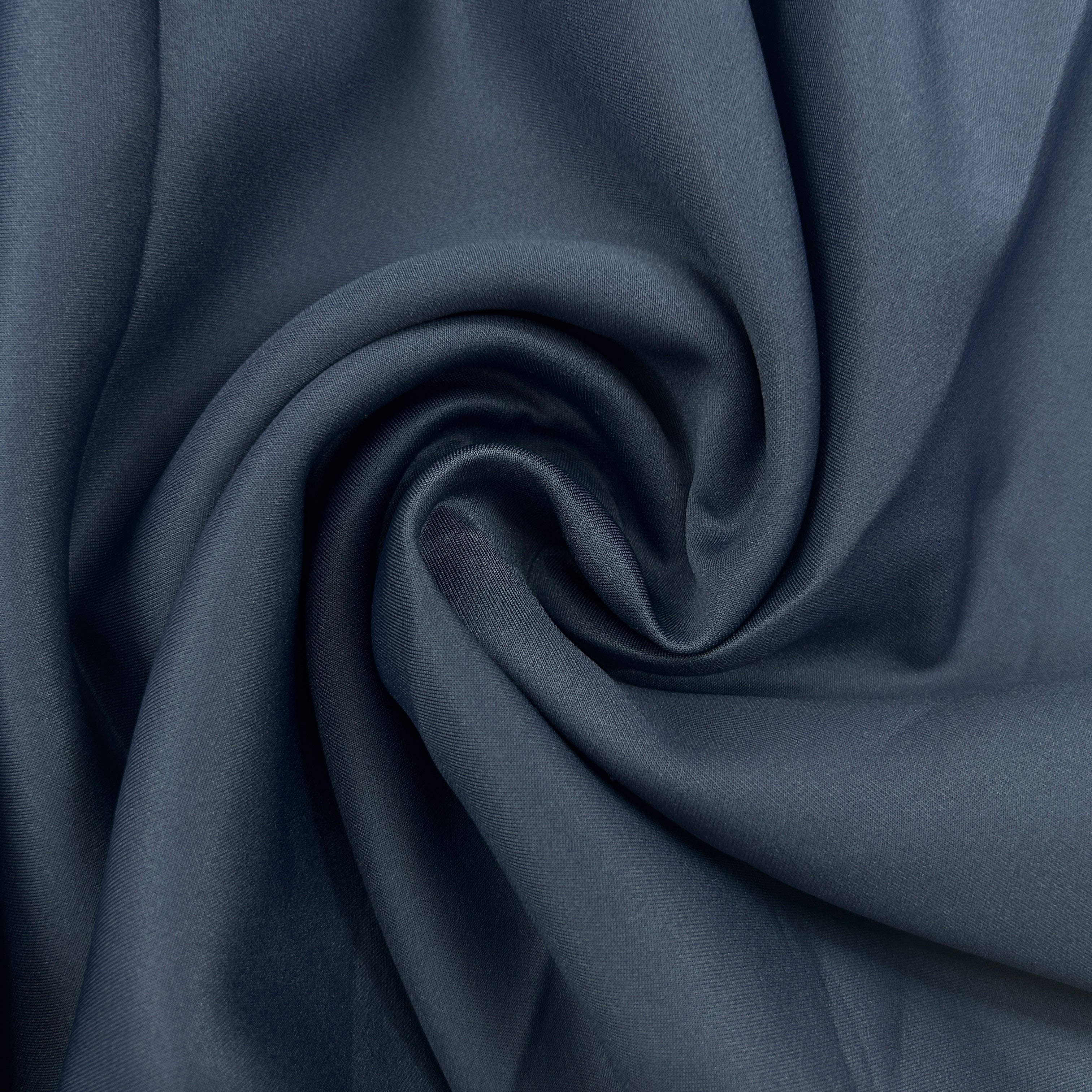 A close-up of draped fabric in a muted slate blue color, arranged in a spiral pattern to show the material's texture and drape.