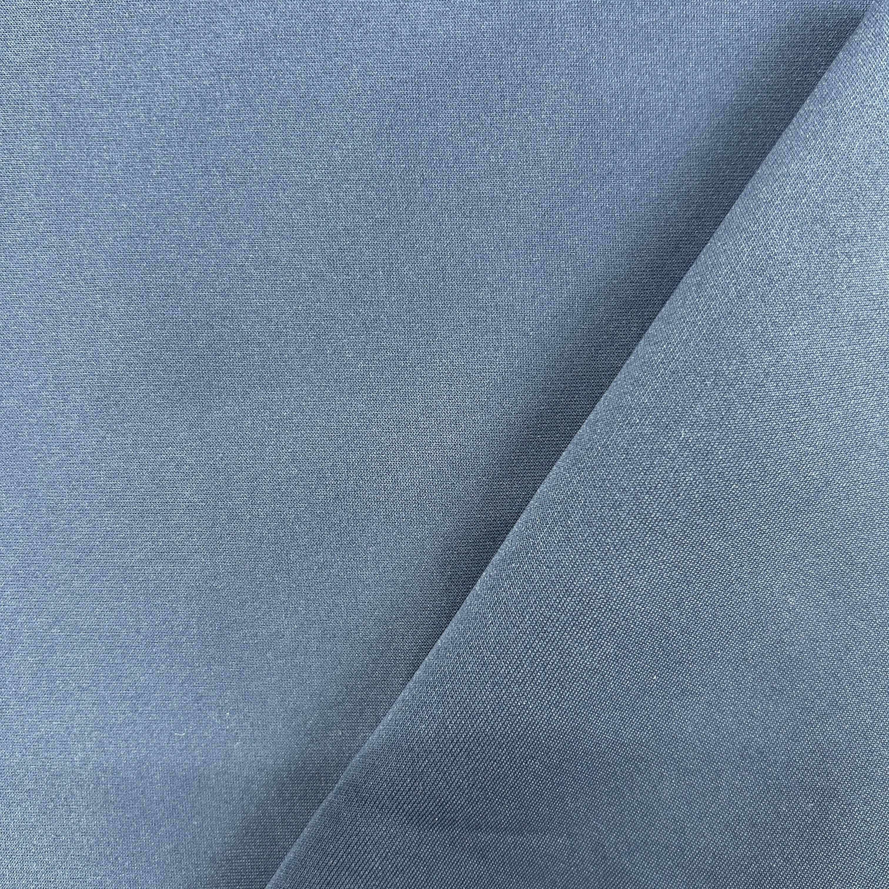 A close-up of a dusty slate blue fabric, showing a fine twill texture and a diagonal fold.