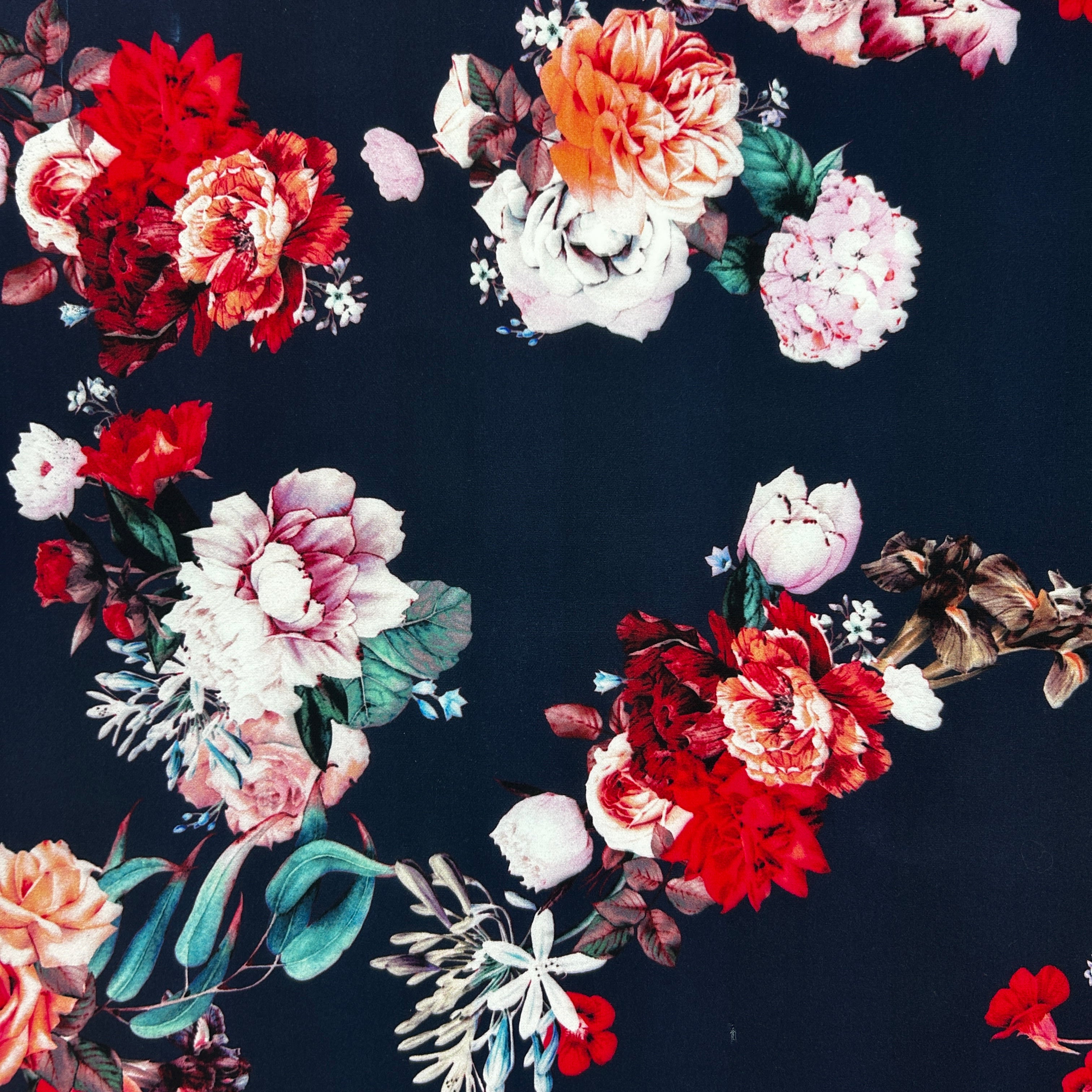 A close-up of a dark navy fabric with a vintage floral print featuring large peonies and roses in red, pink, white, and muted green.