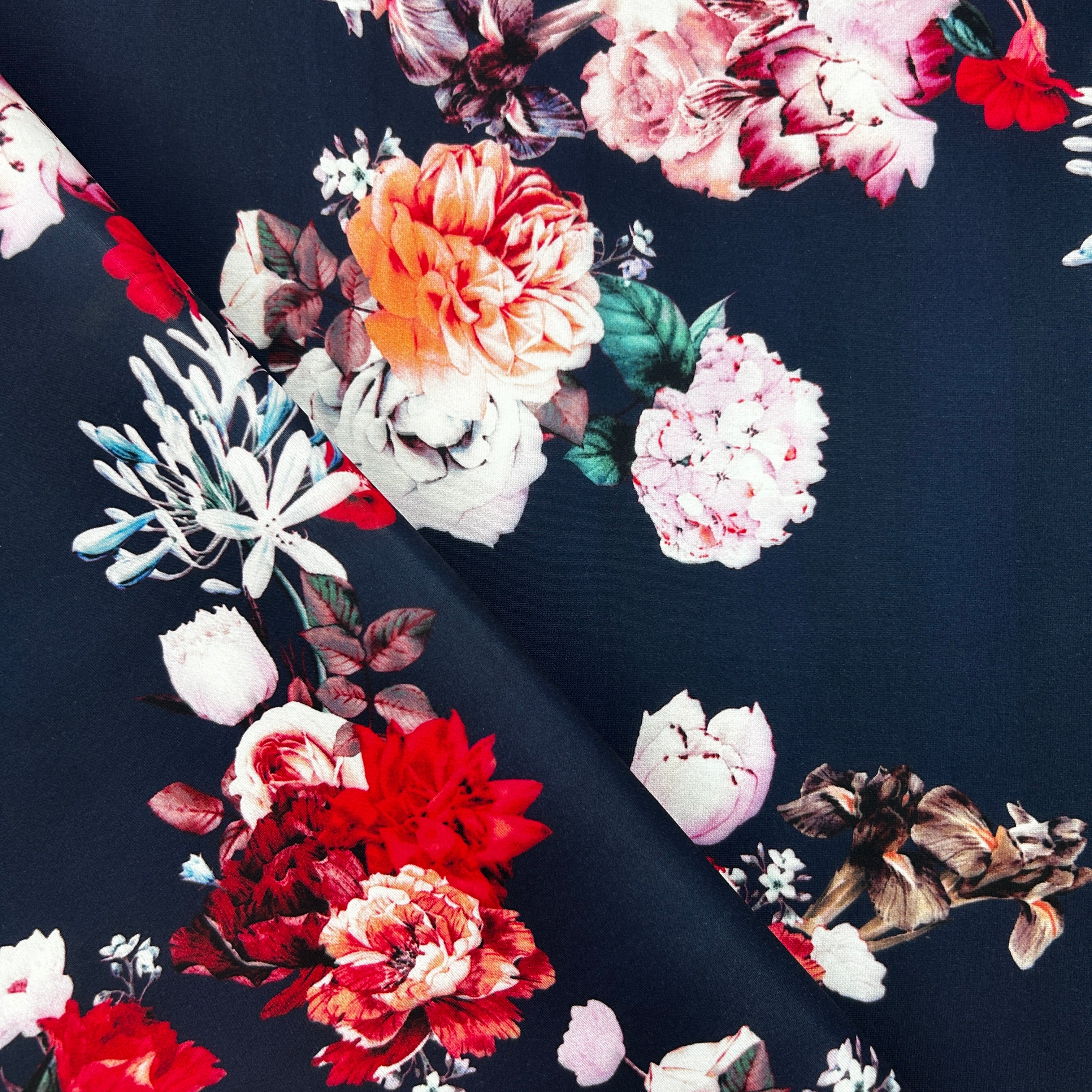A close-up of dark navy floral fabric with large printed flowers in red, pink, white, orange, and green, arranged diagonally with one folded corner revealing the material.