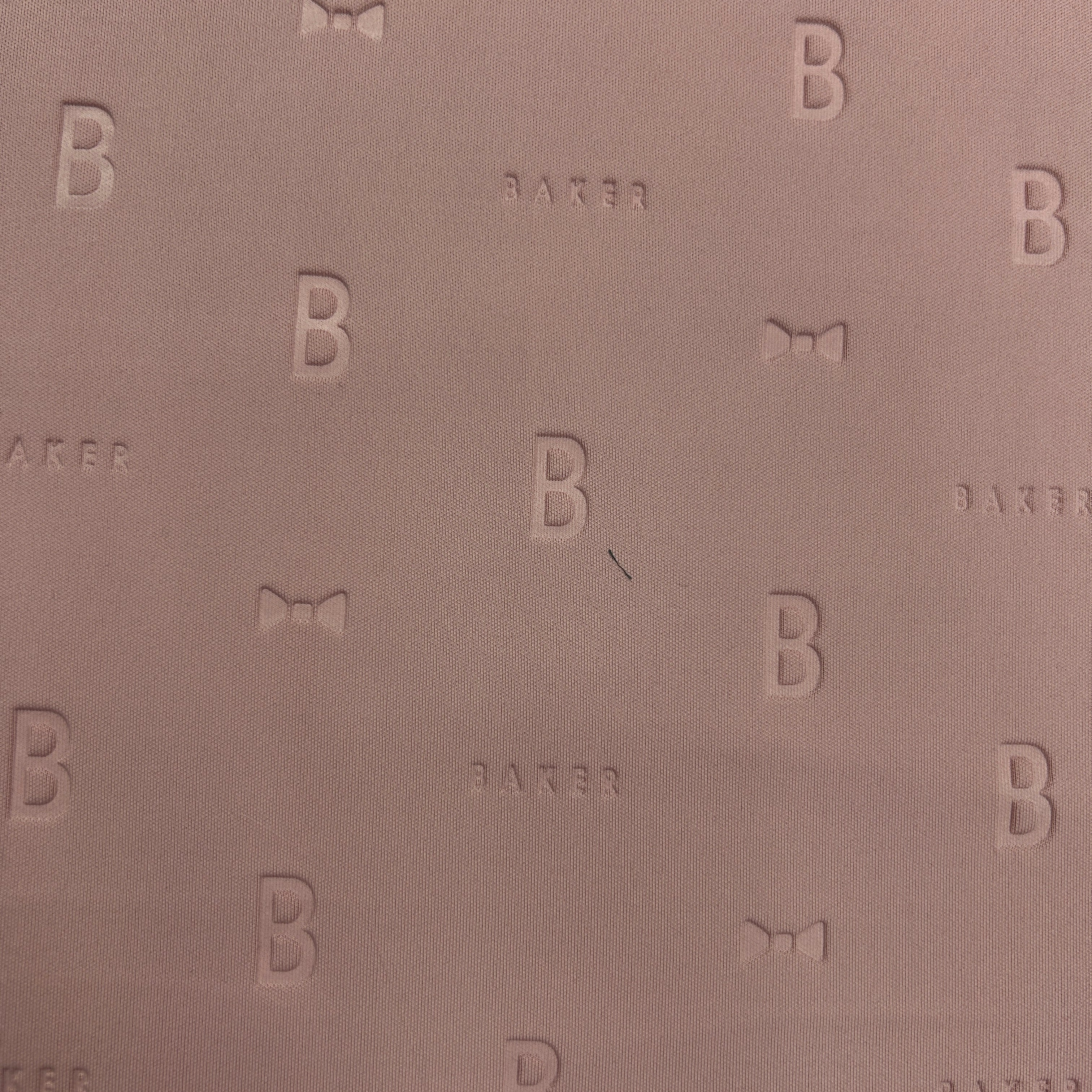 Close-up of mauve 3D Ted Baker thick scuba jersey fabric with embossed 'B' and 'BAKER' logo pattern.