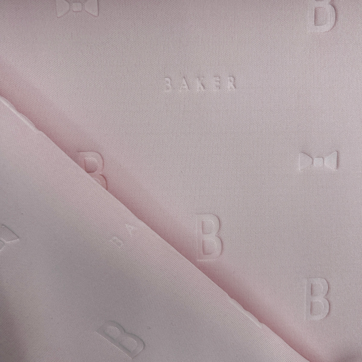 Close-up of pink 3D Ted Baker thick scuba jersey fabric with embossed B letters and bows.