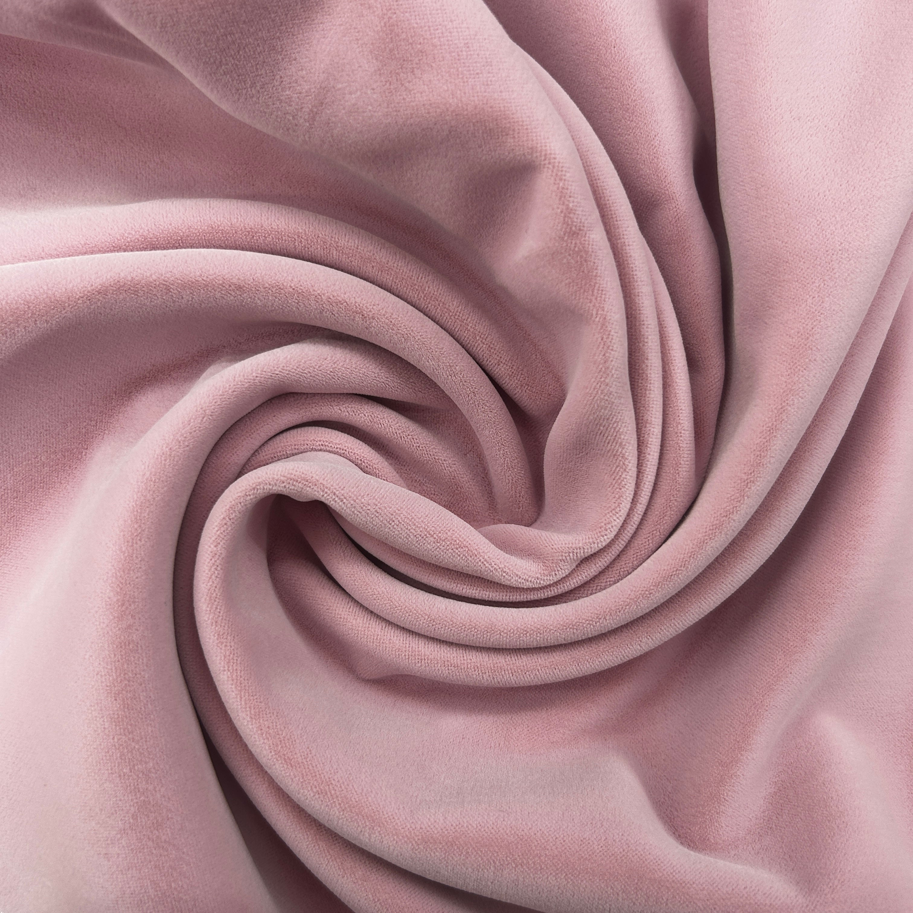 A close-up of draped dusty pink velvet fabric arranged in a spiral pattern, showing its soft texture and sheen.