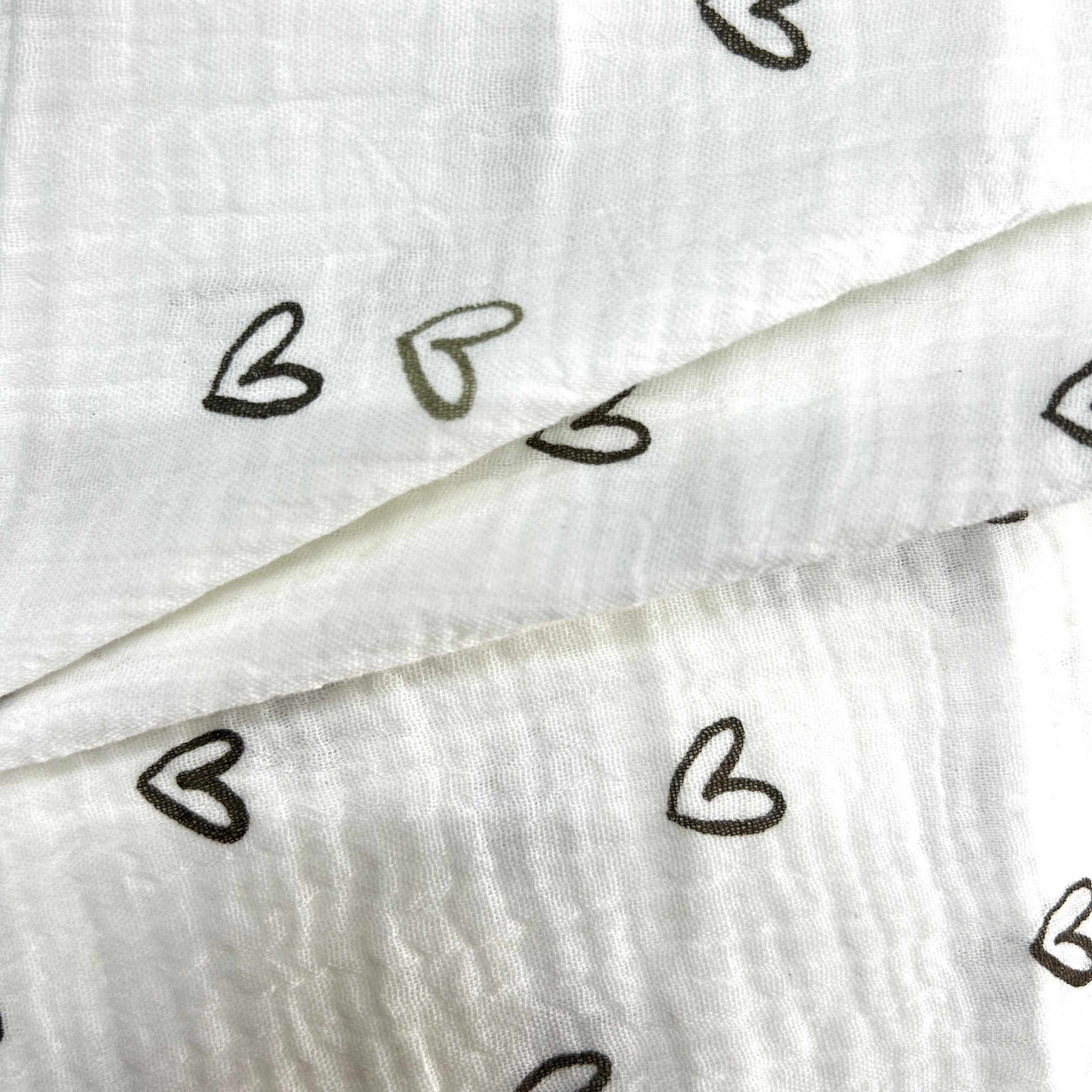 White crinkled gauze fabric with a repeating pattern of small hand-drawn black hearts, folded to show its soft texture.