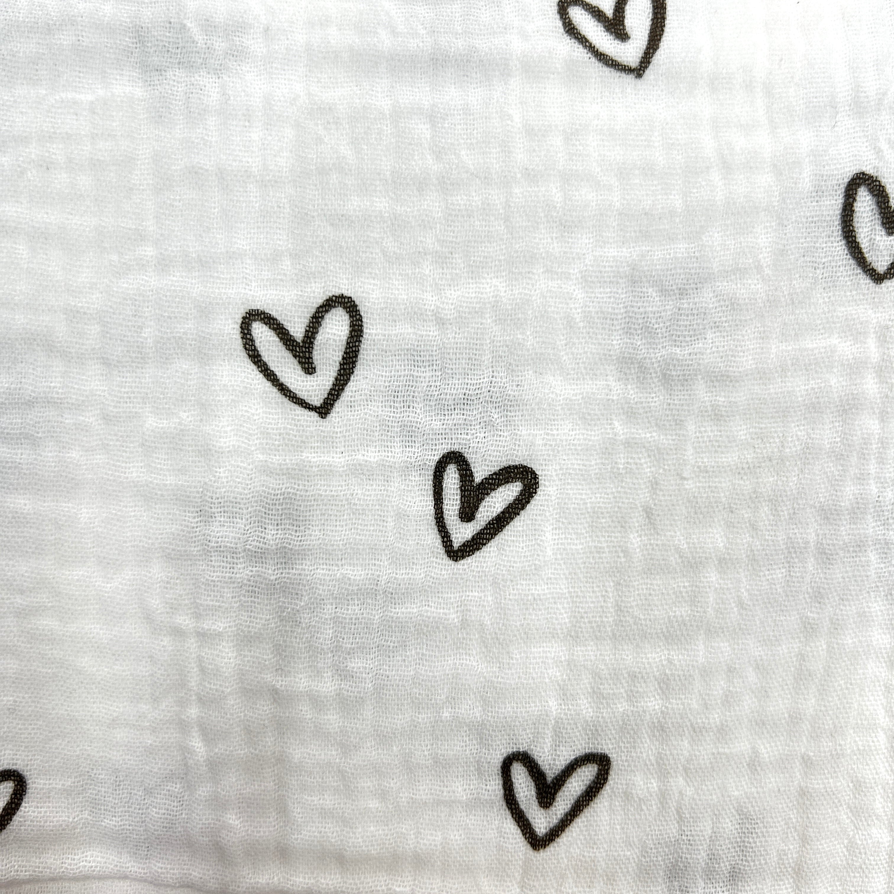 White muslin fabric with a black hand-drawn heart pattern, shown in a close-up texture view.