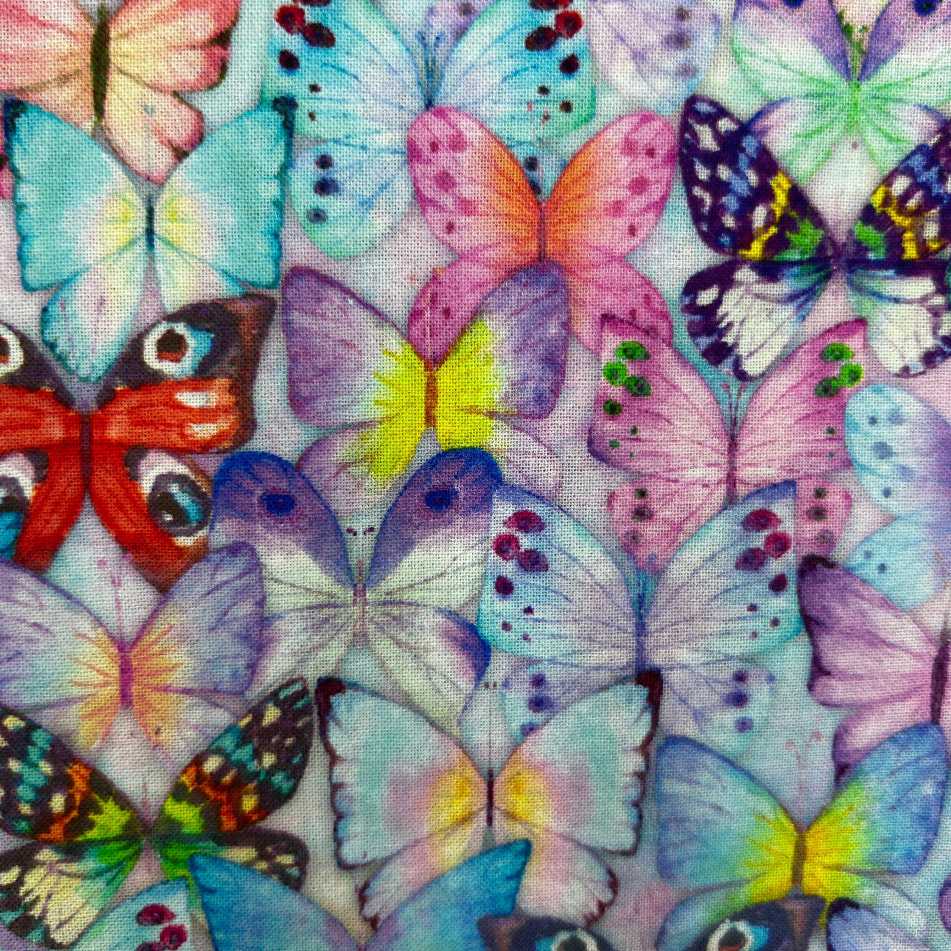A close-up of fabric featuring a dense, colorful print of various butterflies in shades of pink, purple, blue, green, orange, and red on a light background.