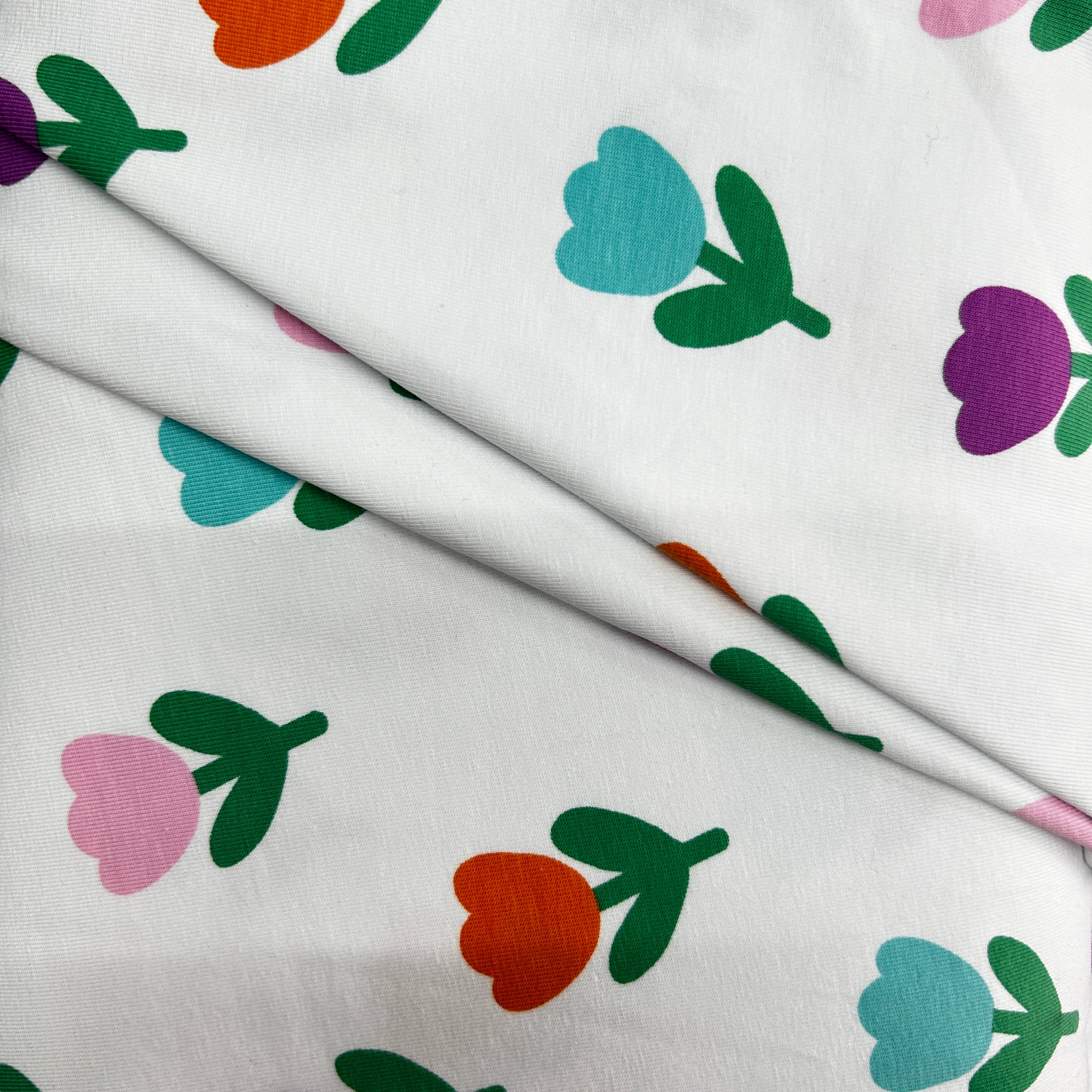 White fabric with a colorful tulip pattern, featuring pink, orange, light blue, and purple flowers with green leaves, draped with a diagonal fold.