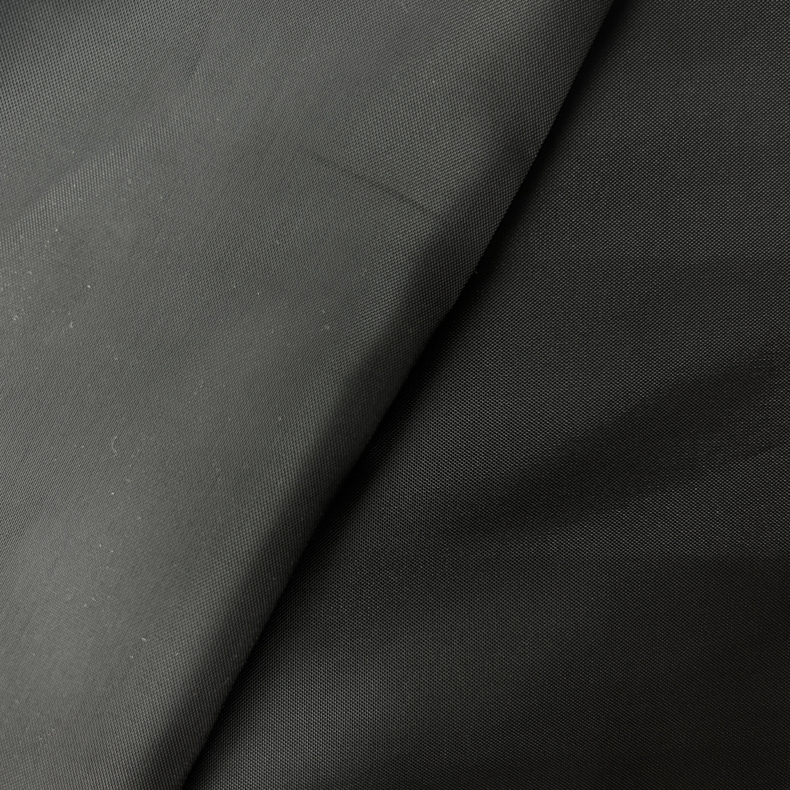 A close-up of dark charcoal gray fabric with a fine woven texture and soft folds.