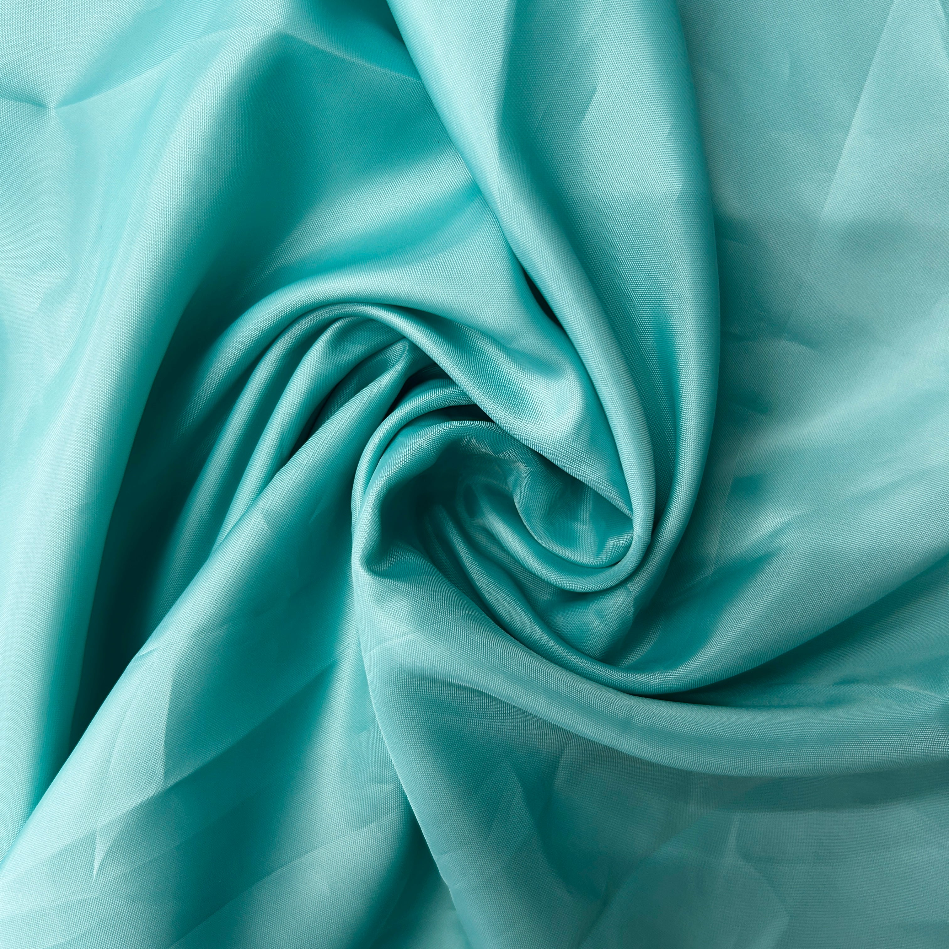A close-up of draped satin fabric in a light aqua or turquoise color, arranged in elegant swirls and folds.