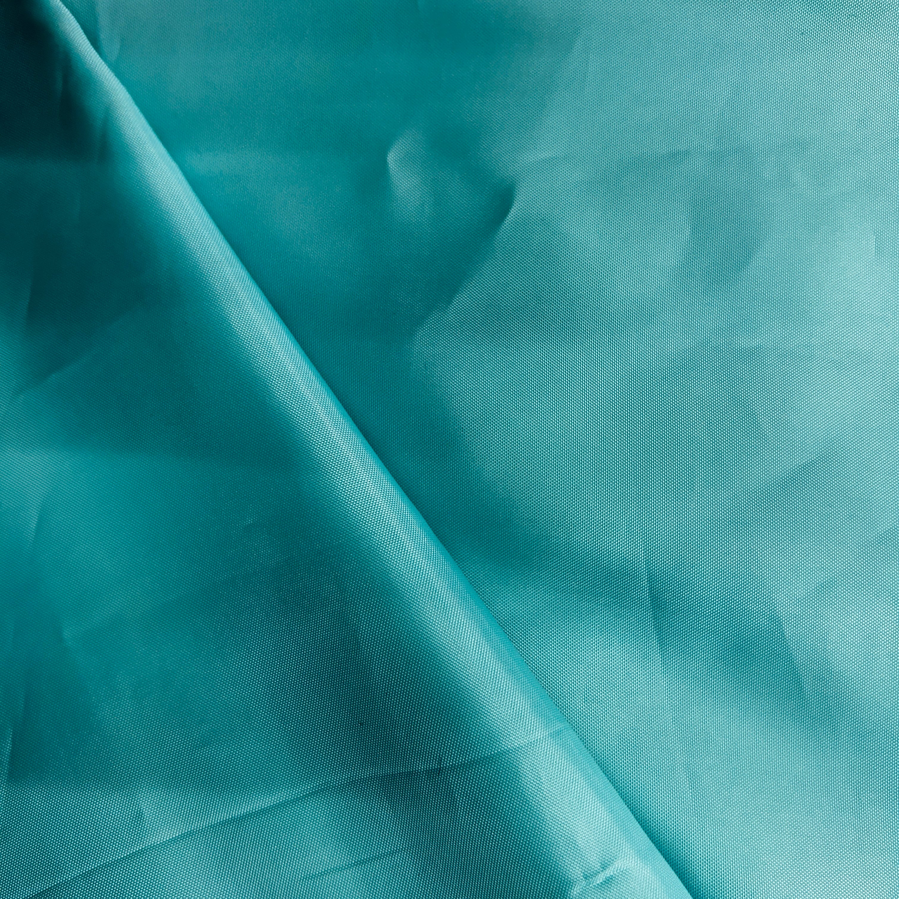 A close-up of teal fabric with a diagonal fold creating soft shadows across the surface.
